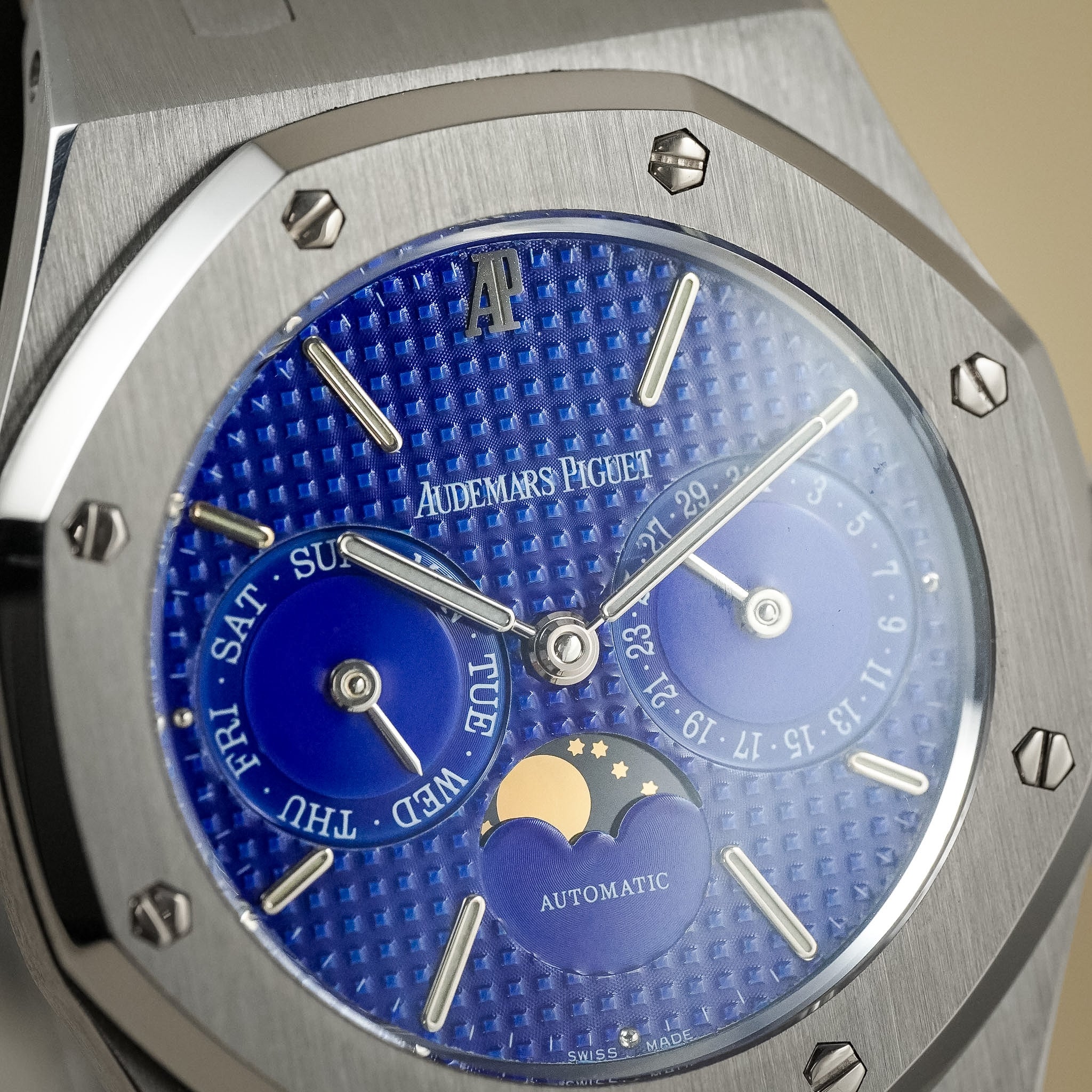 Close-up of an Audemars Piguet Royal Oak Automatic watch with a textured blue dial, silver-toned case, and day/date/moon complications.