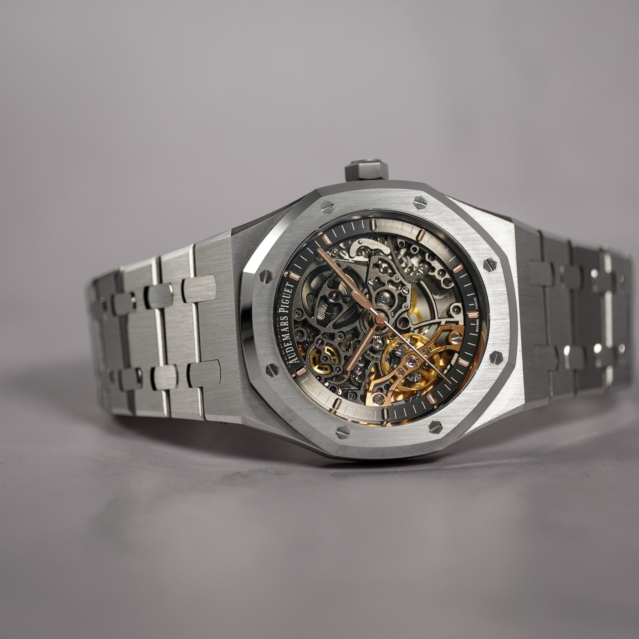 A luxury skeleton watch with a brushed stainless steel octagonal case and integrated bracelet, showcasing a detailed gold and silver mechanical movement through a black dial.