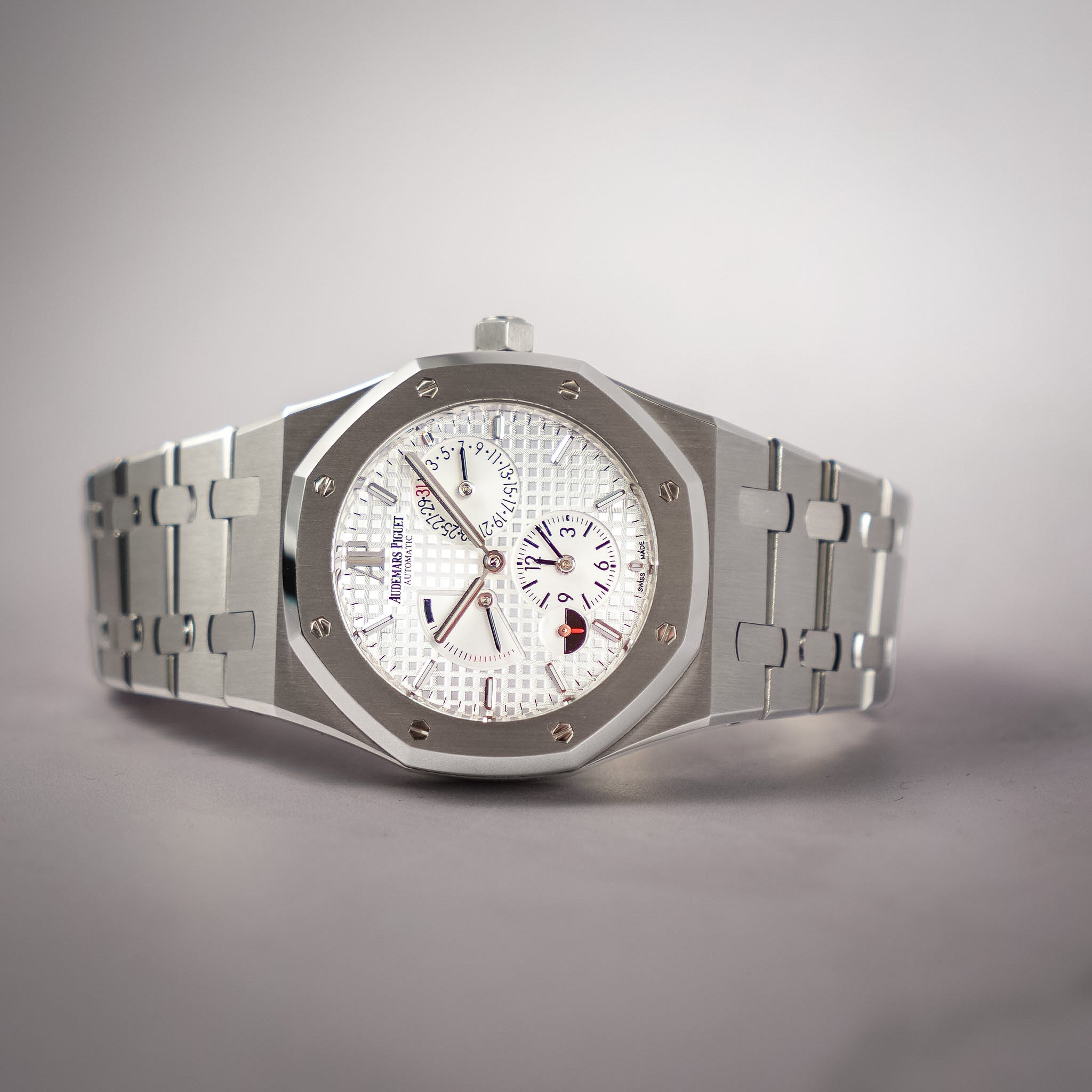 An Audemars Piguet Royal Oak watch with a silver stainless steel octagonal case, white textured dial, and matching silver integrated bracelet, photographed on a neutral gray background.