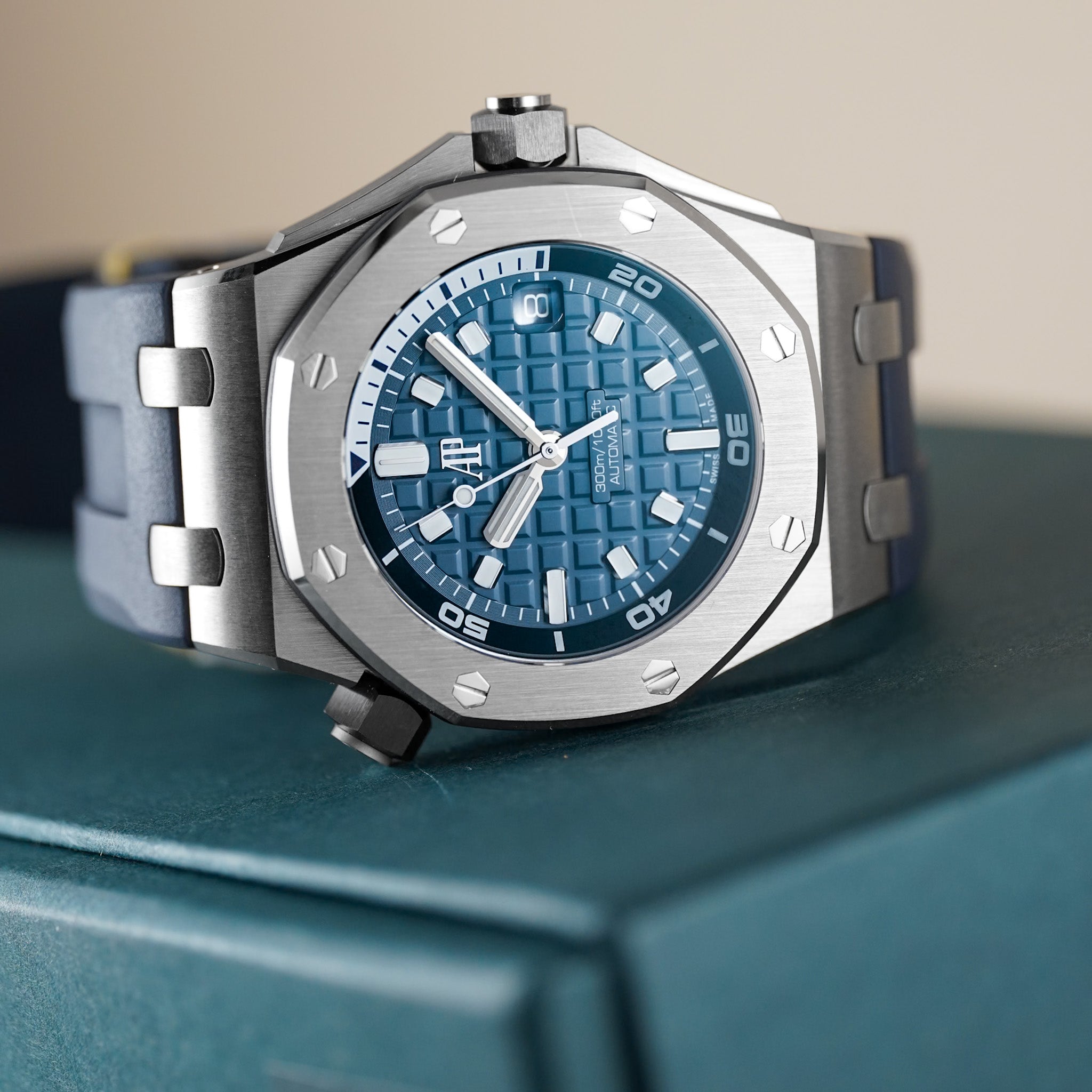 An Audemars Piguet Royal Oak Offshore Diver in navy blue with a steel case and rubber strap laying on its side atop a dark green box