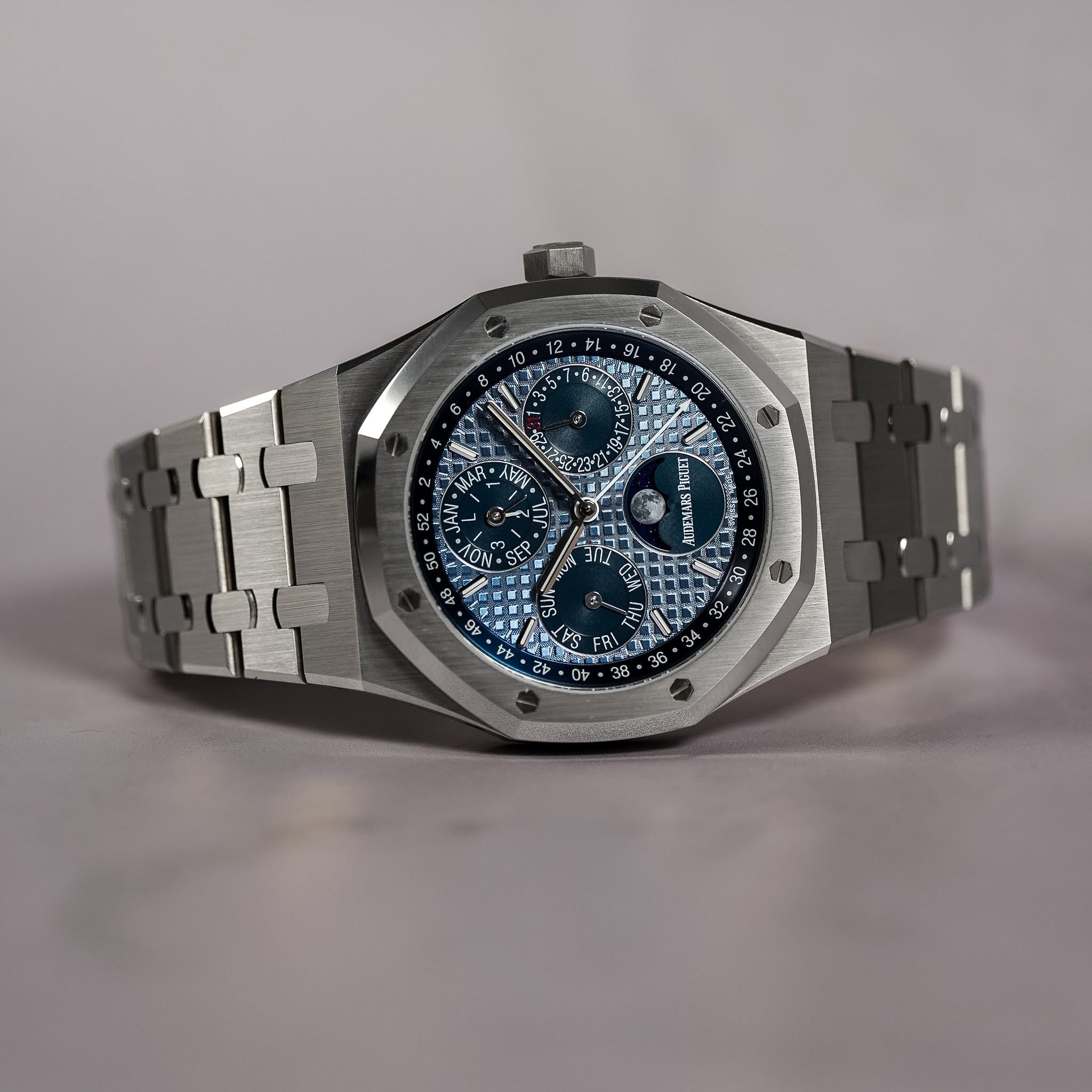 An Audemars Piguet Royal Oak watch with a silver stainless steel octagonal case and link bracelet, featuring a textured blue dial with silver sub-dials and markers.
