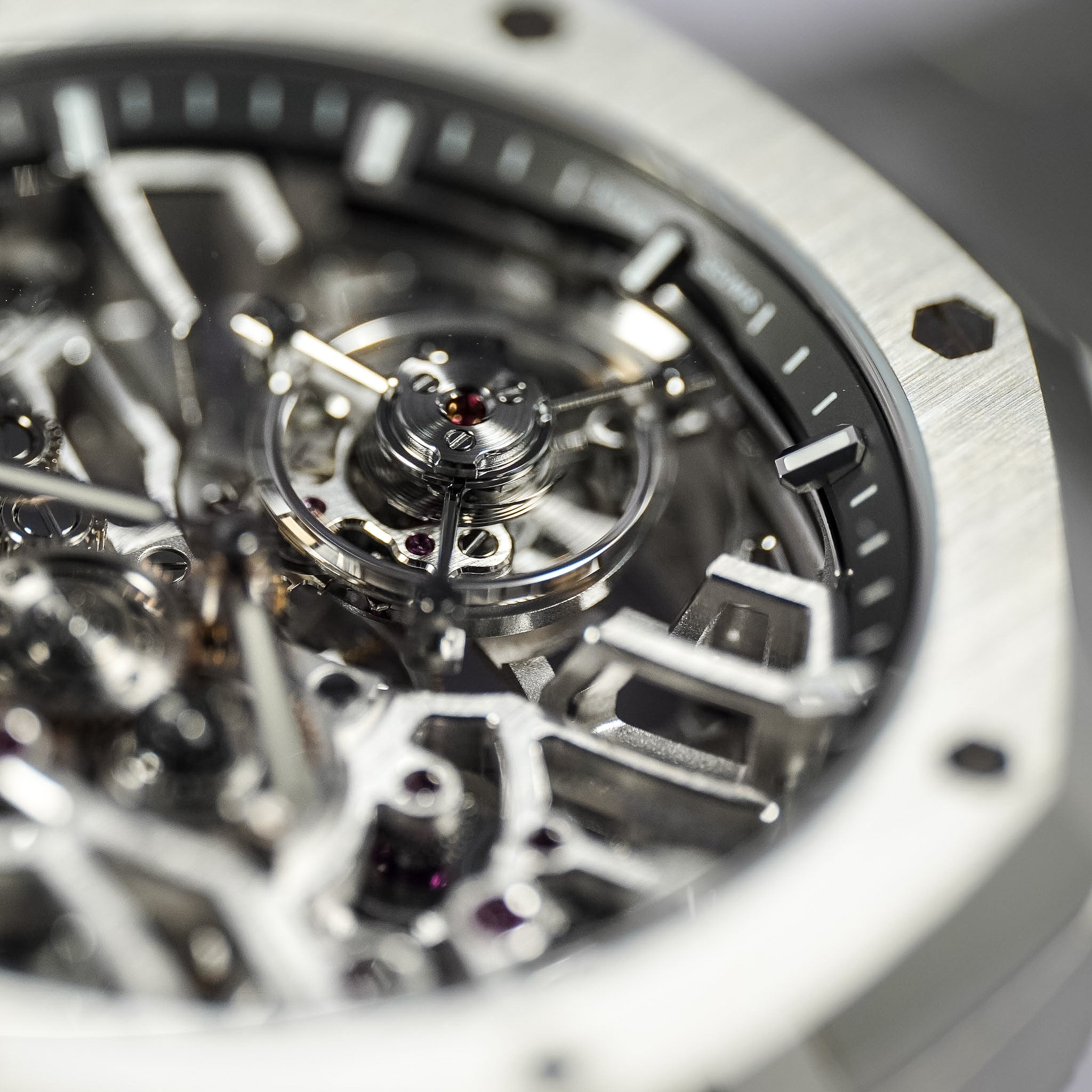 Close-up of a skeleton watch face showing polished silver-tone mechanical gears and a black dial, with part of the brushed silver case visible at the edges.