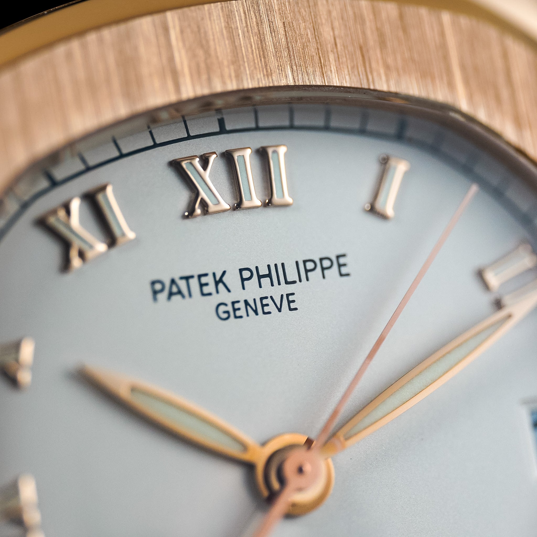 Close-up of a Patek Philippe wristwatch dial with Roman numeral hour markers, a pale blue-gray face, and gold-tone hands and markers.
