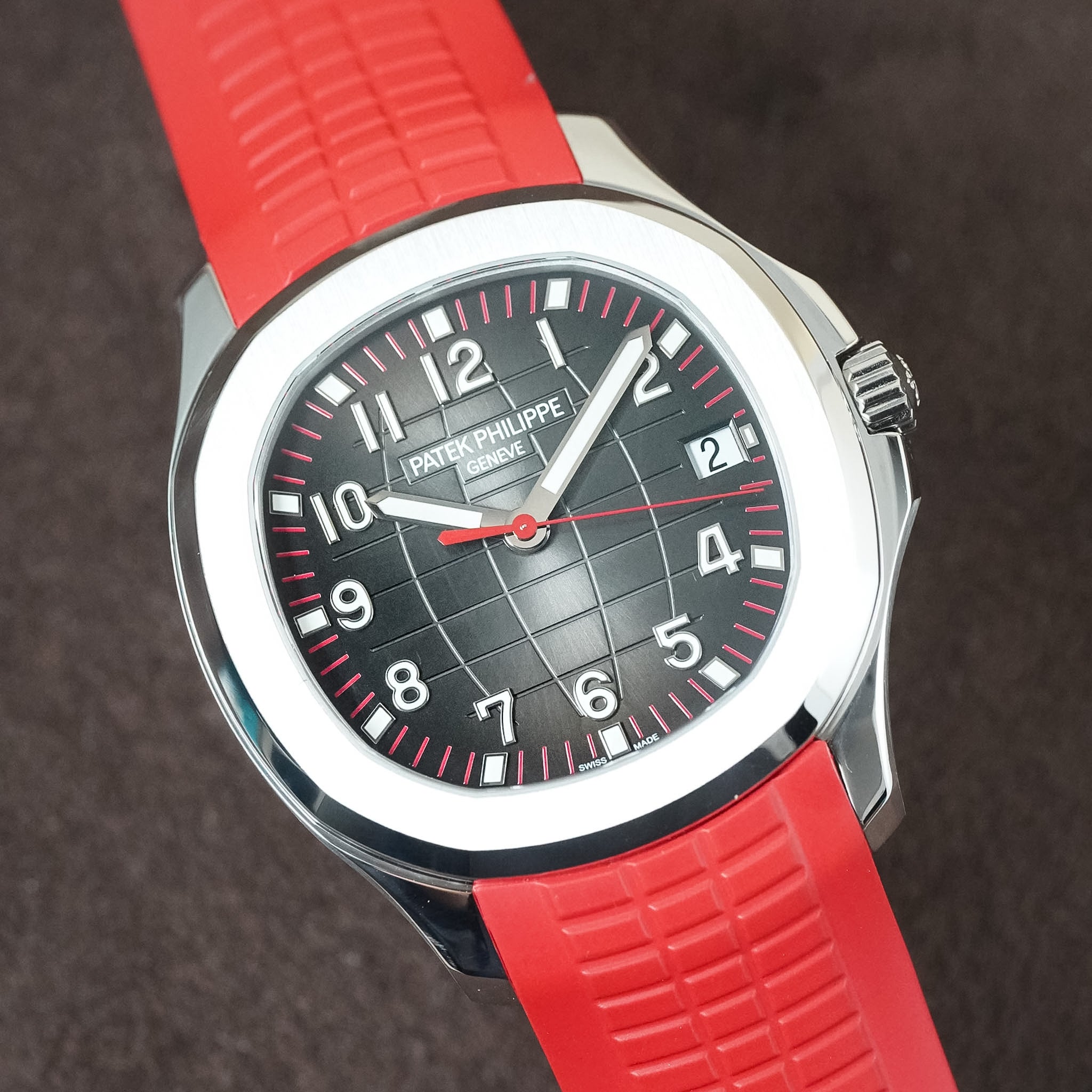 Patek Philippe Nautilus watch with a black textured dial, white Arabic numerals, and a vibrant red silicone strap, shown in a close-up shot against a dark textured background.