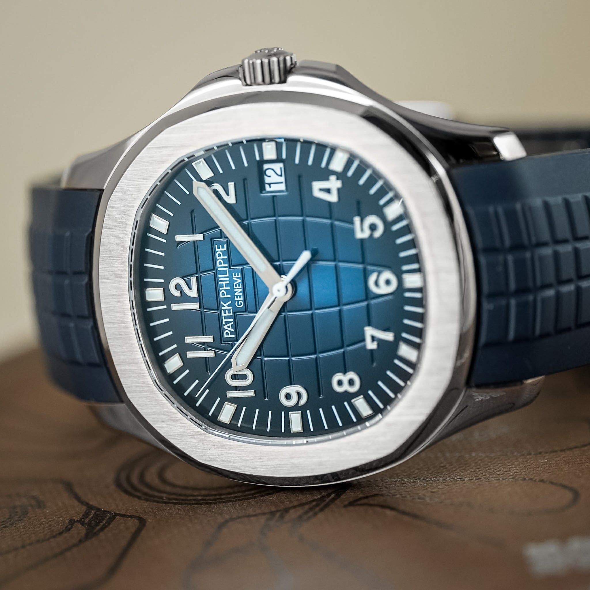 A Patek Philippe Aquanaut in white gold with a blue dial and blue rubber strap laying sideways on a brown Patek Philippe box