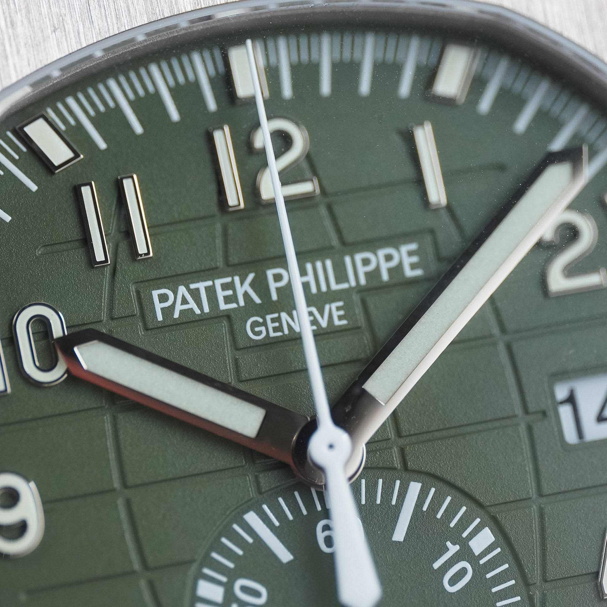 Close-up of a Patek Philippe Geneve watch dial in olive green with silver-tone hands, white hour markers, and a date window.