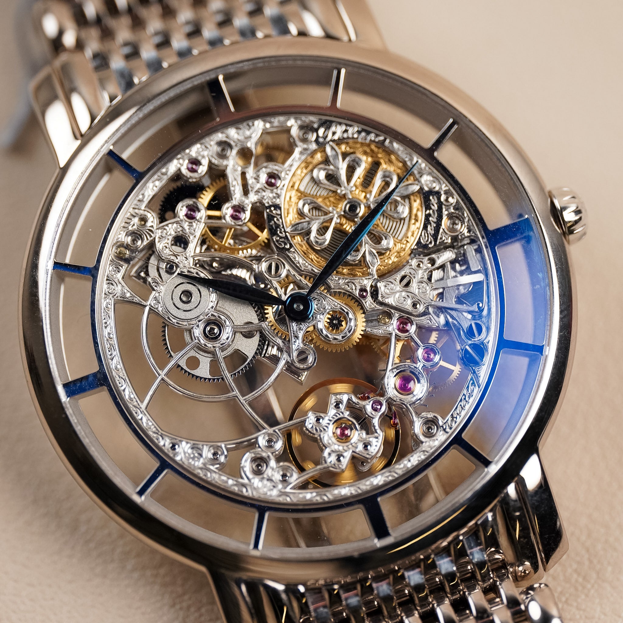 A white gold Patek Philippe watch with an intricately decorated skeletonized movement on a white gold mesh bracelet, shot against a neutral cream background