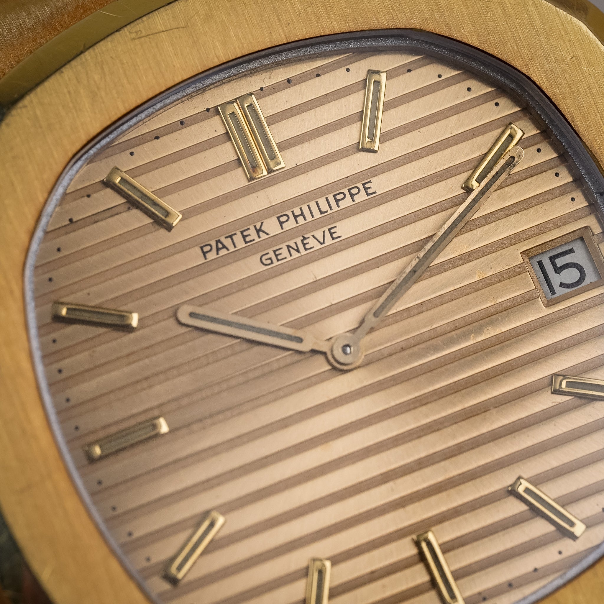 Closeup of a yellow gold Patek Philippe Nautilus with a gold-tone dial, yellow gold case and bezel, gold hands and hour markers, and a date window at 3 o'clock showing "15".