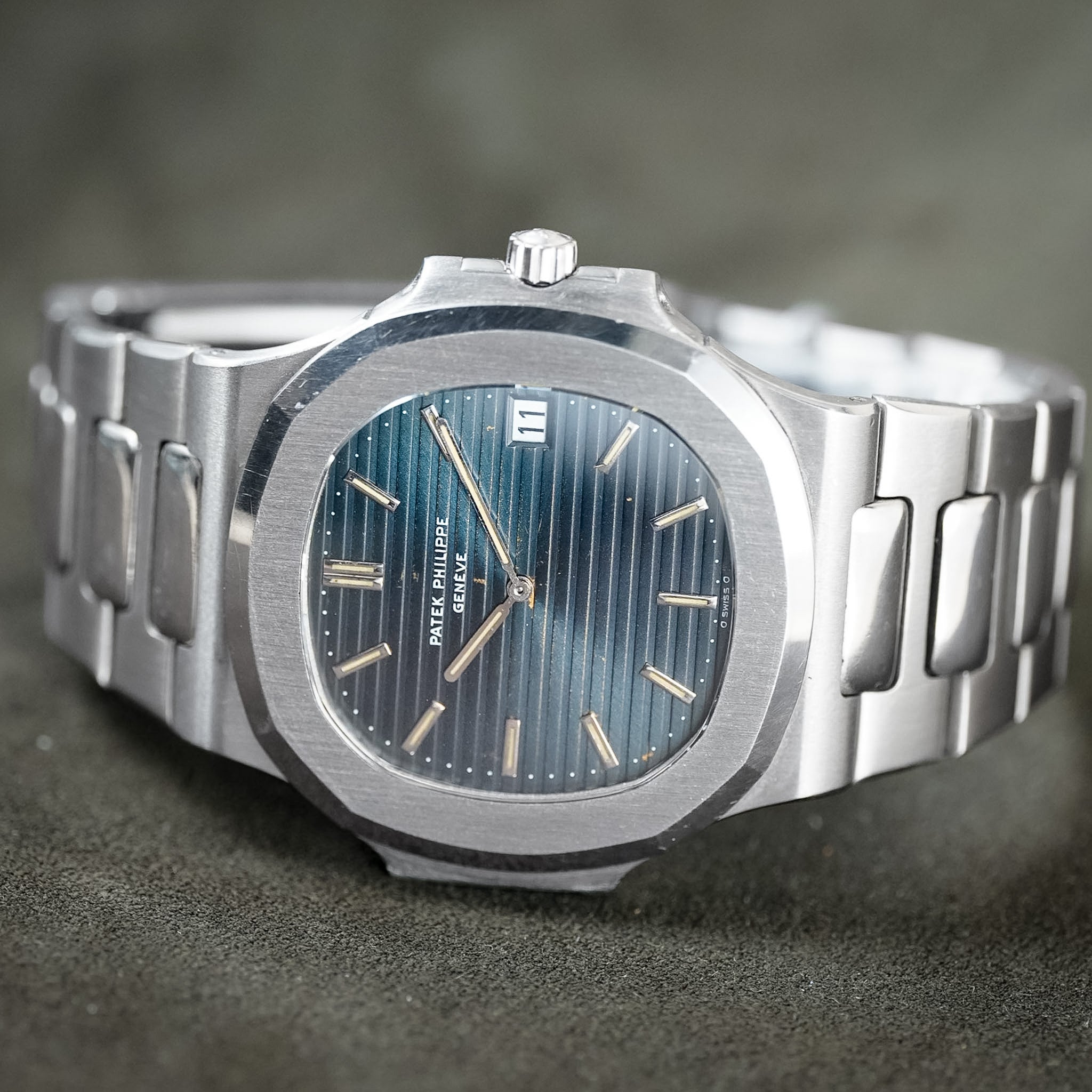 A silver stainless steel wristwatch with an octagonal bezel, a blue sunburst dial, and gold-tone indices, photographed close-up on a dark textured surface.