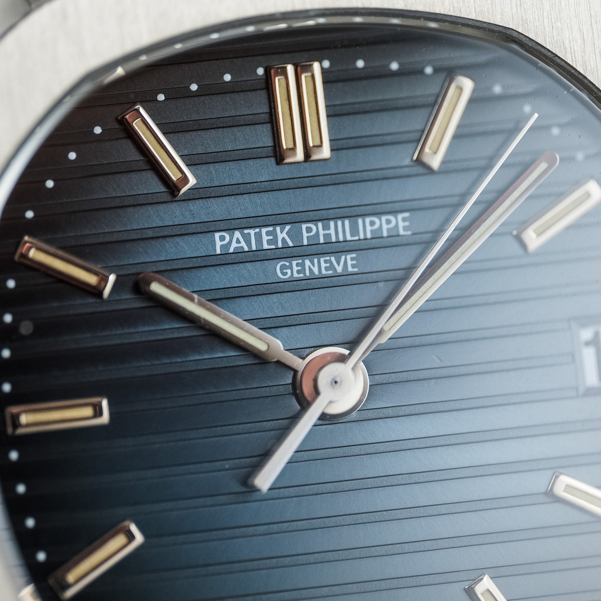 Close-up of a Patek Philippe Geneve watch dial with a dark blue textured background, white gold baton indices, and white gold hands.