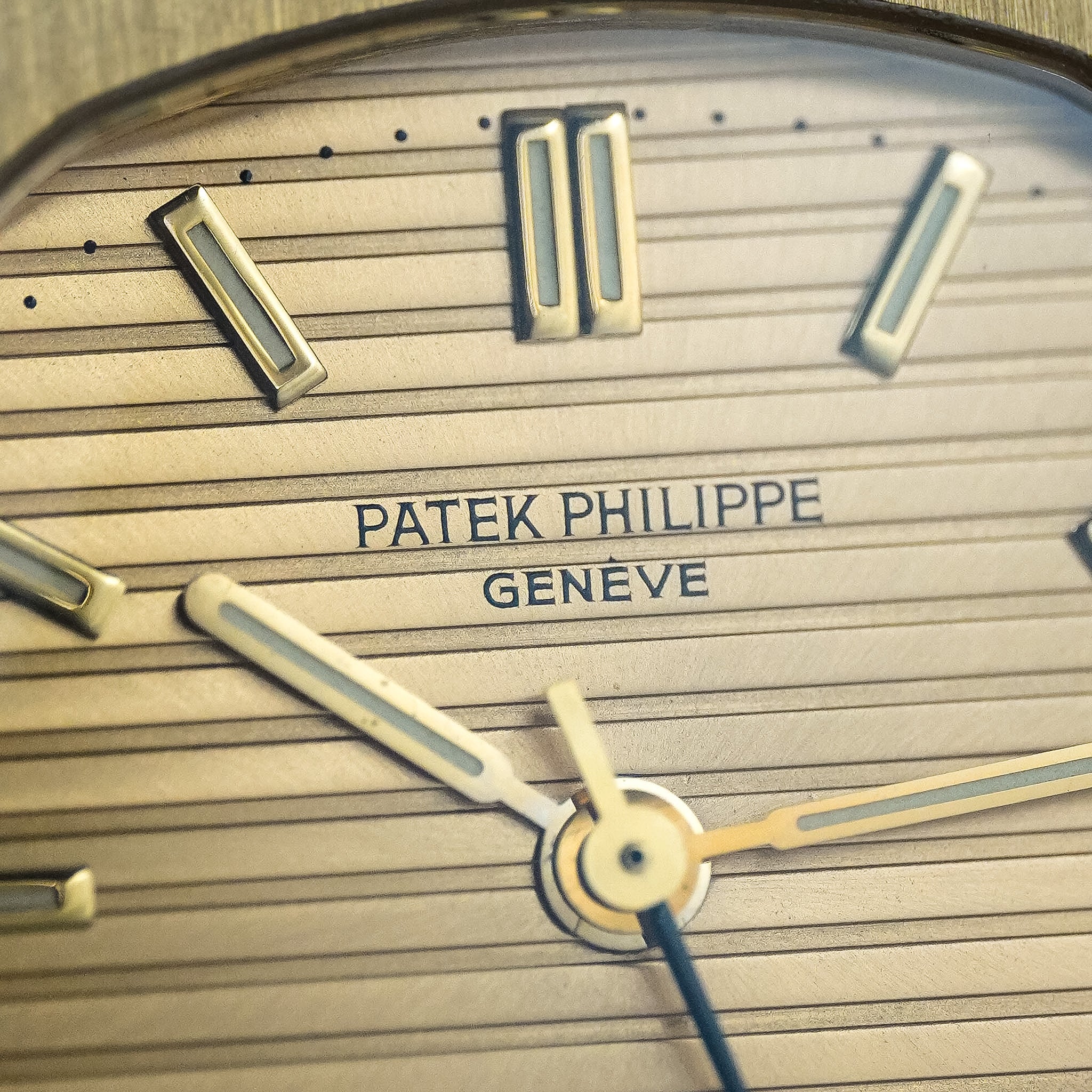 Close-up of a Patek Philippe watch dial with gold baton markers, gold hands, and a gold textured dial.