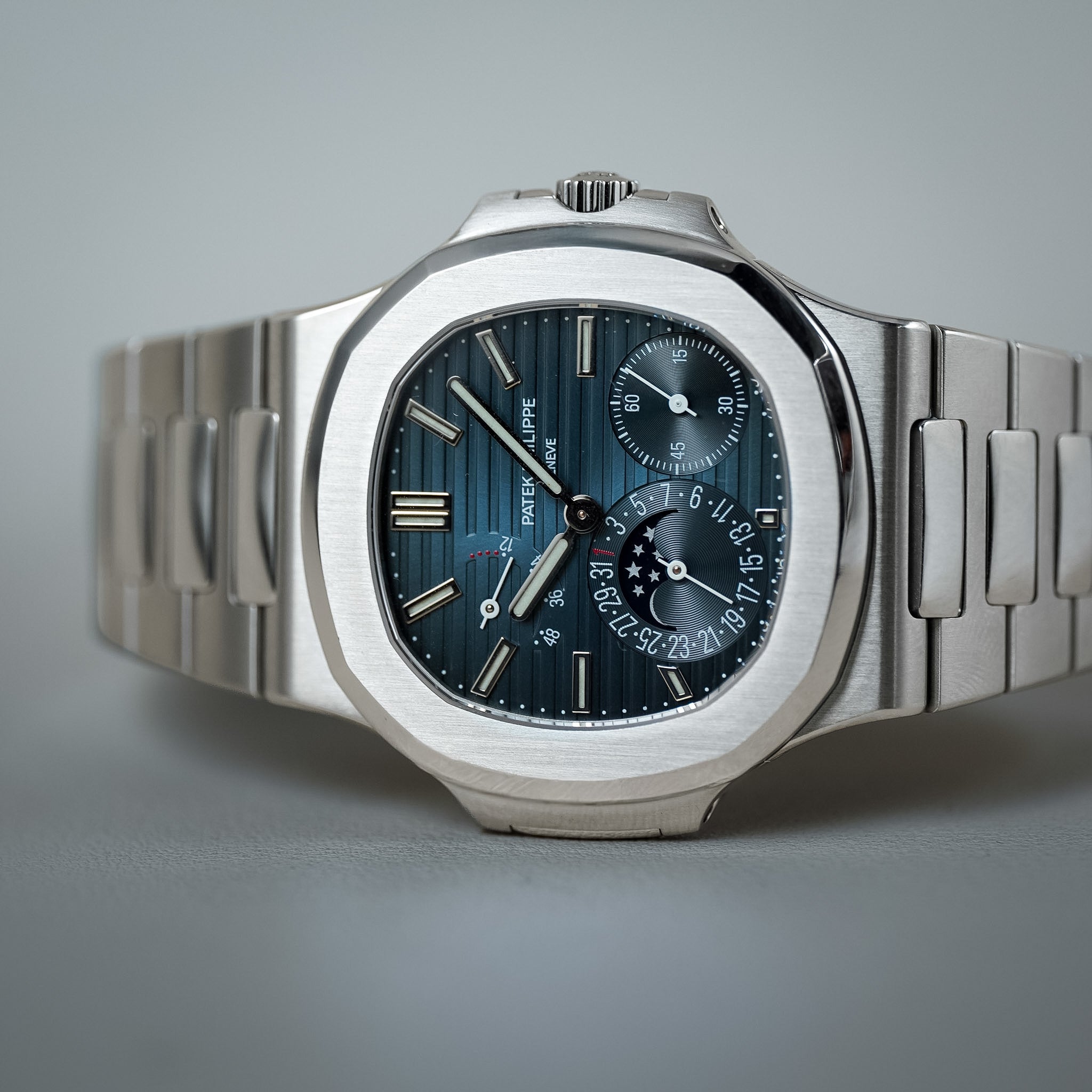 A luxury stainless steel wristwatch with an octagonal bezel, a dark blue sunburst dial, and a matching metal link bracelet, photographed on a neutral gray background.