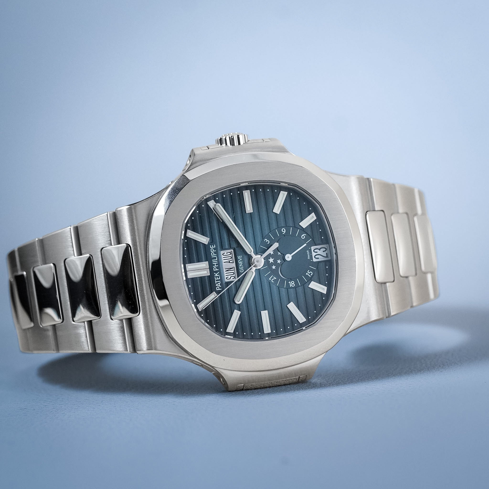 A stainless steel wristwatch with an octagonal bezel, a blue sunburst dial, and a matching steel link bracelet, photographed on a light blue background.