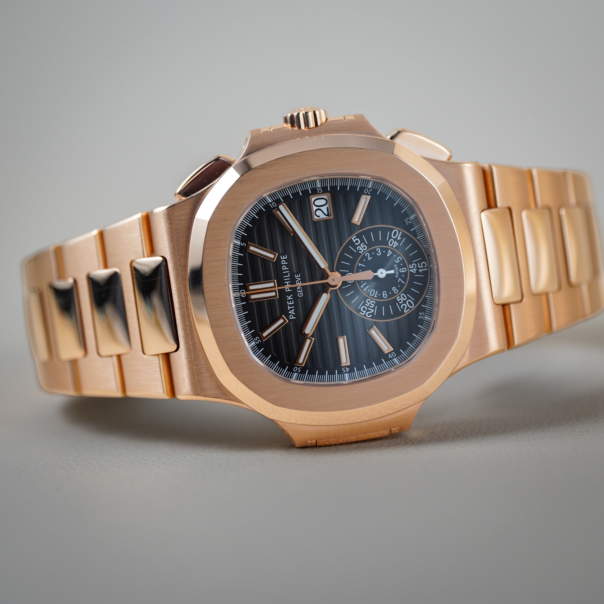 A luxury wristwatch with a rose gold-toned stainless steel case and integrated bracelet, featuring a dark grey dial with silver and rose gold accents, photographed on a neutral gray background.