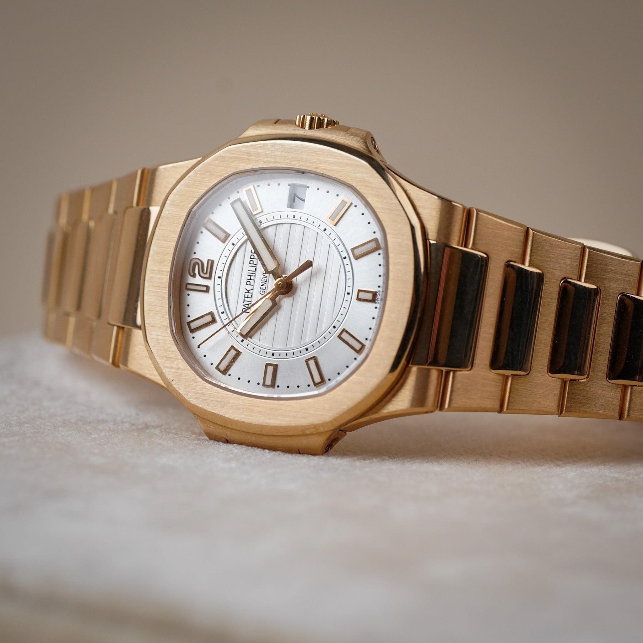A rose gold Patek Philippe ladies wristwatch with a textured white dial, rose gold bracelet, and rose gold hands and hour markers, resting sideways on a cream colored surface
