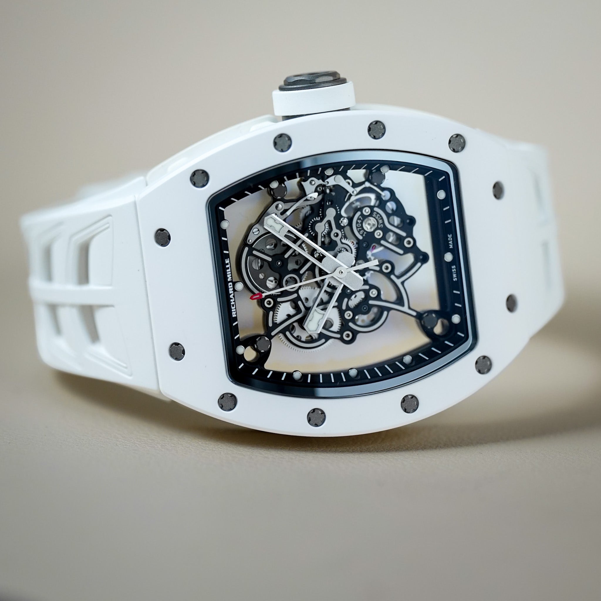 A white Richard Mille wristwatch with a skeleton dial showing the inner mechanical movement, photographed on a neutral beige background.
