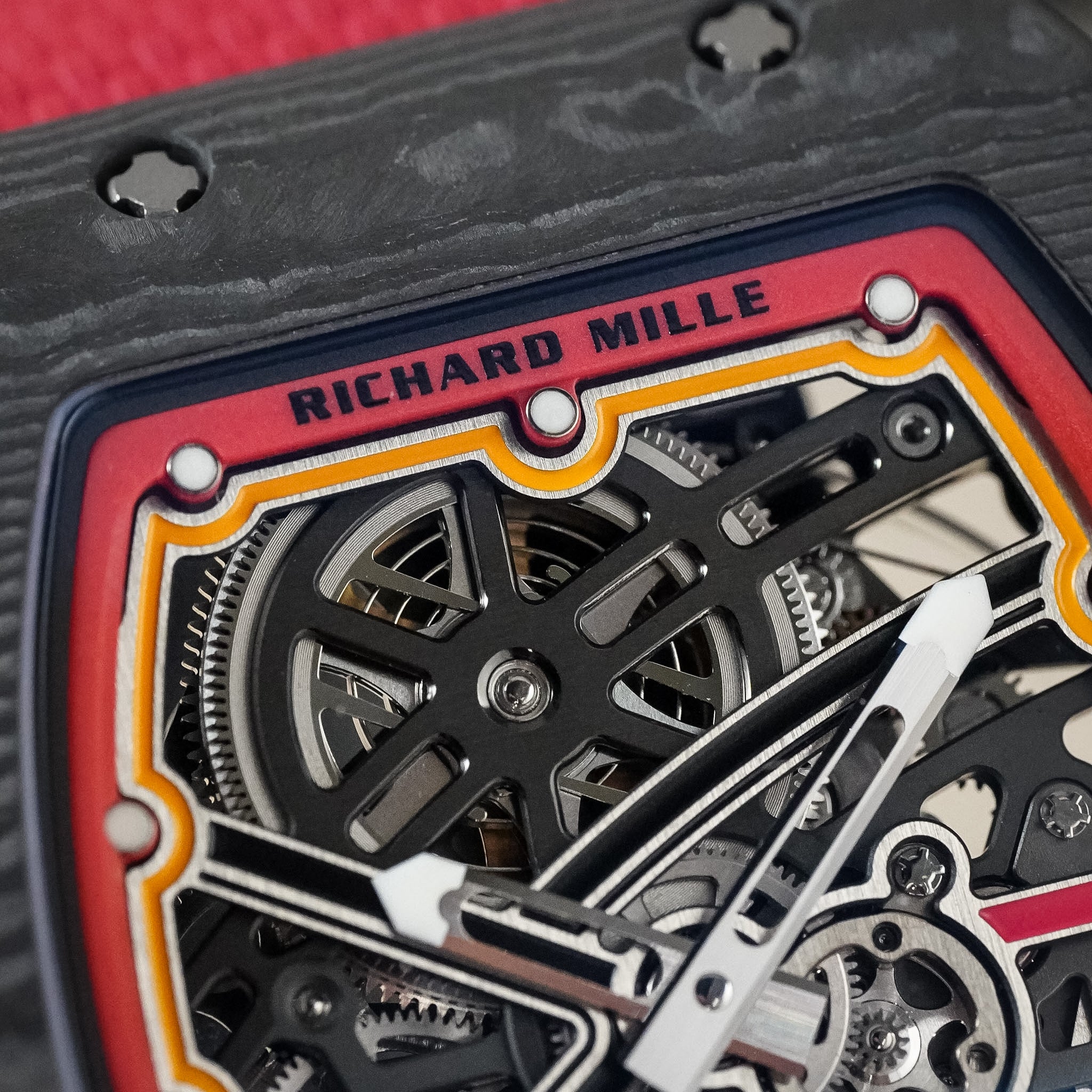 Closeup of a Richard Mille watch dial. The watch has a layered carbon fiber case, skeletonized dial, and red and yellow accents.