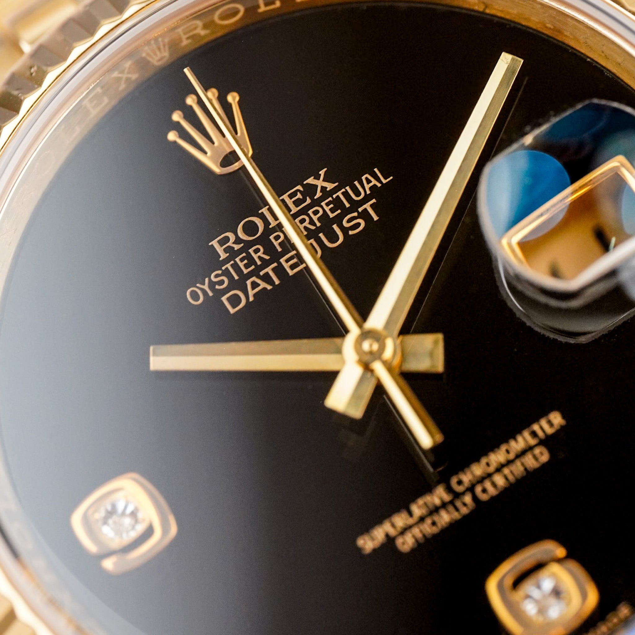 Closeup of a yellow gold Rolex Datejust with a fluted bezel, deep black onyx dial, and a date window showing "11"