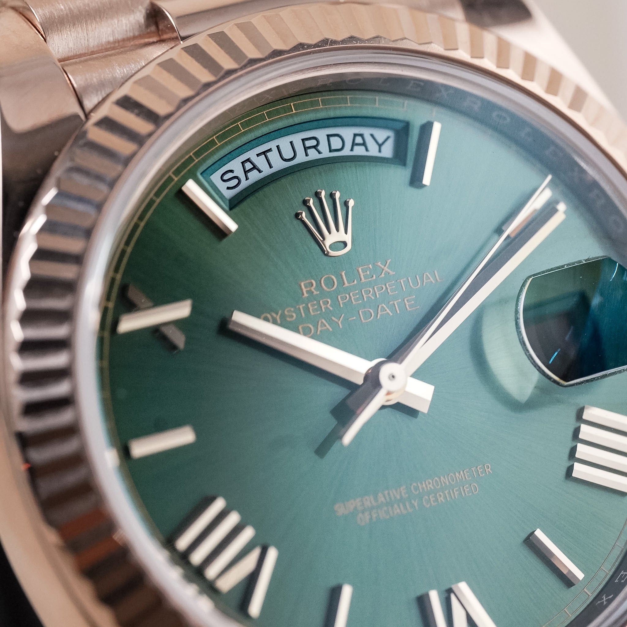 Close-up of a Rolex Oyster Perpetual Day-Date watch with a green dial, rose gold case, fluted bezel, and day-of-week window at the top.