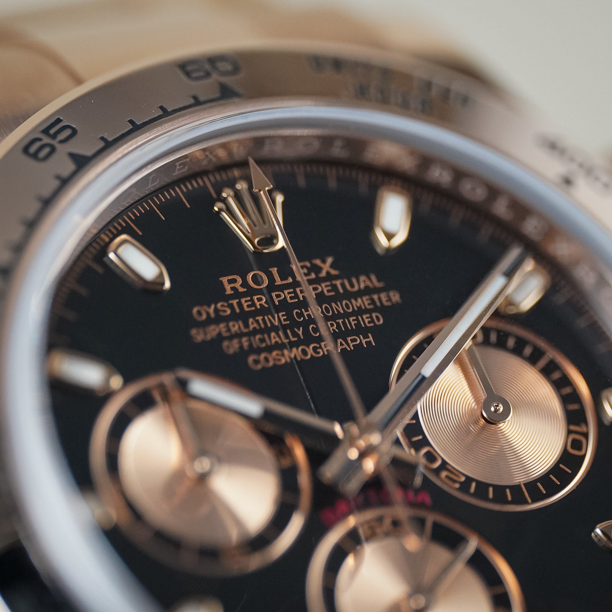 Close-up of a Rolex Oyster Perpetual Cosmograph watch with a black dial, silver-tone bezel, and rose gold-toned subdials and hands.