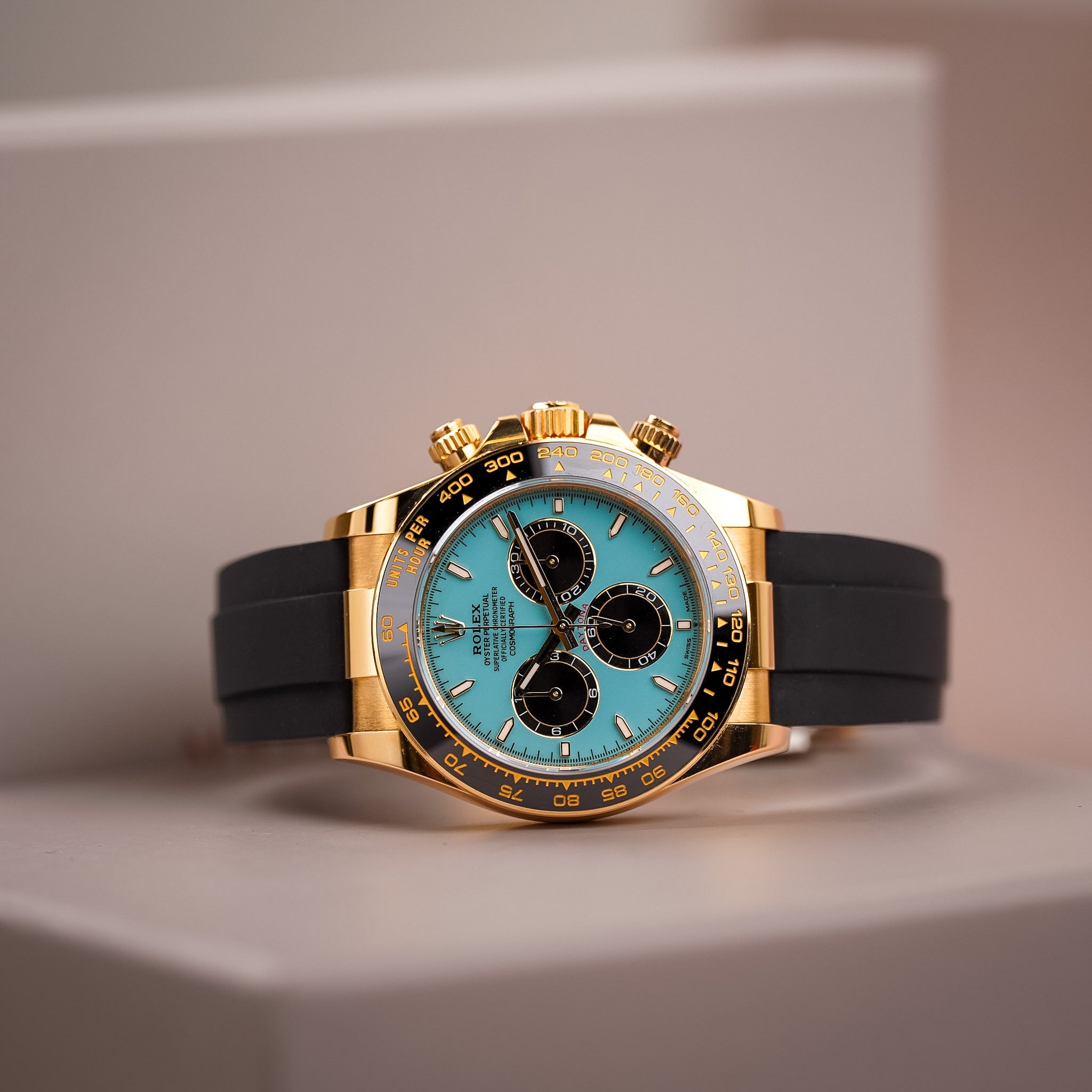 A yellow gold Rolex Daytona with a turquoise dial and black bezel and subdials lying sideways on a white box
