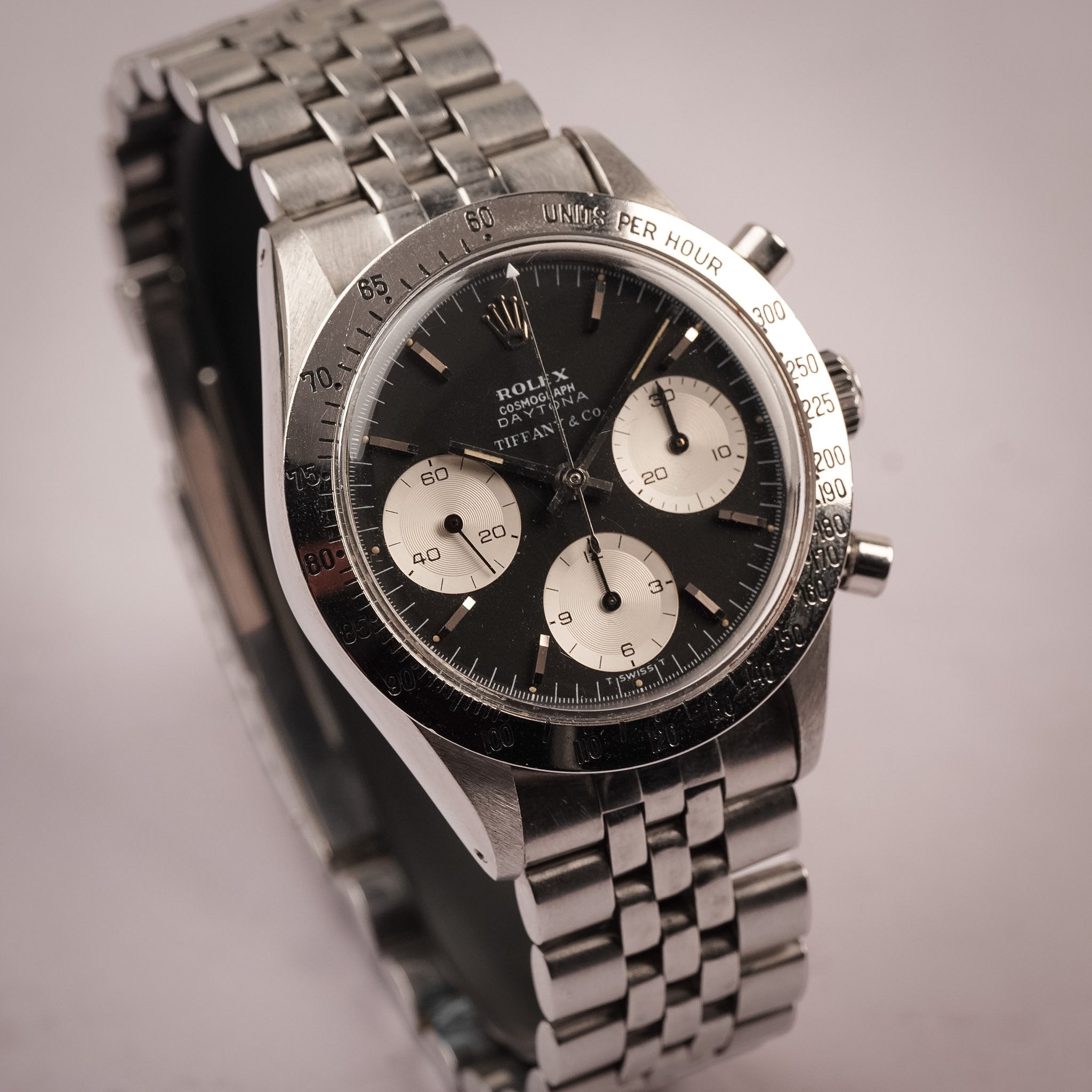 An angled shot of a steel vintage Rolex Daytona with a lack dial, white subdials, steel bezel, and steel bracelet, shot against a light grey background
