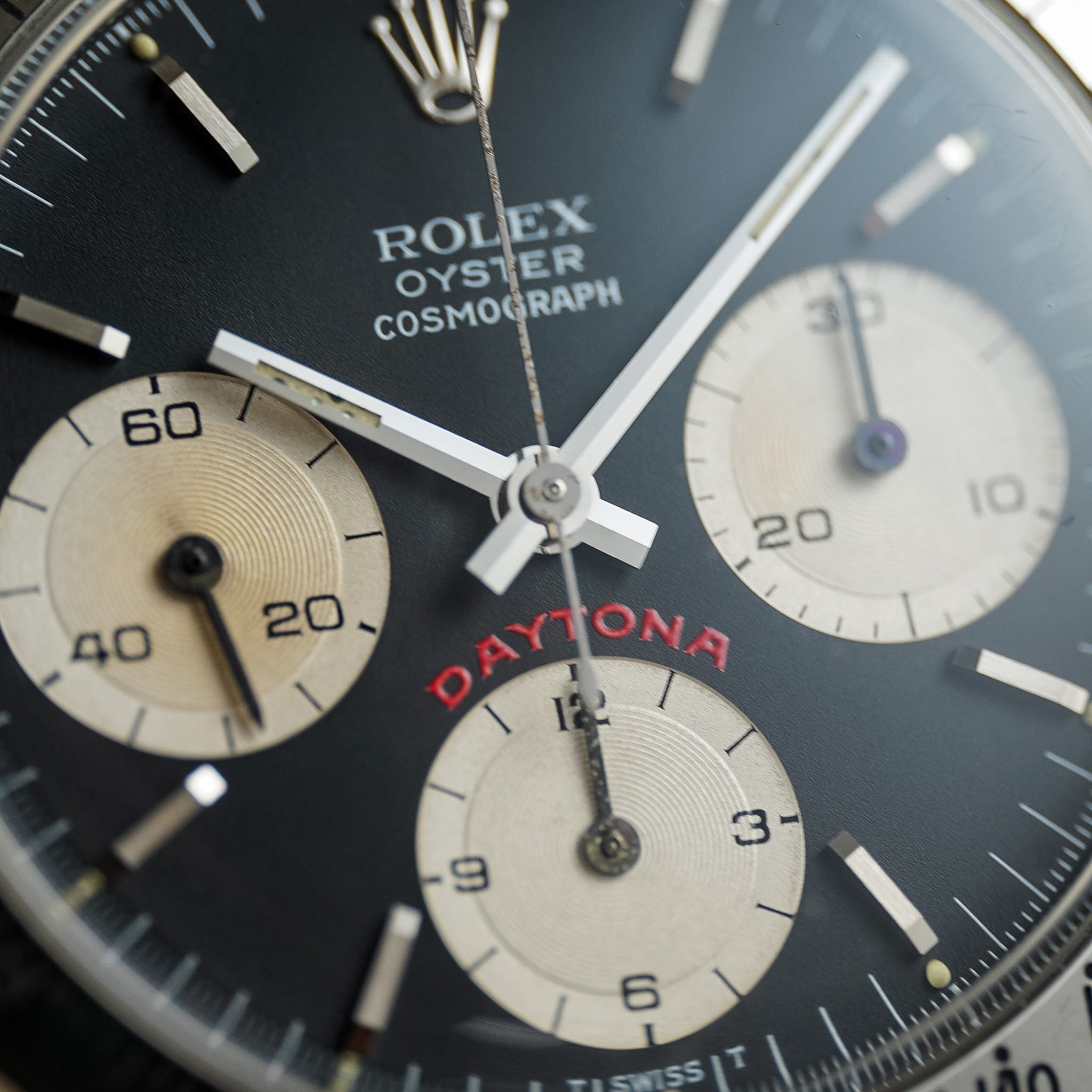 Close-up of a Rolex Daytona Cosmograph wristwatch dial, showing a black main dial with three cream-colored subdials and silver hands.