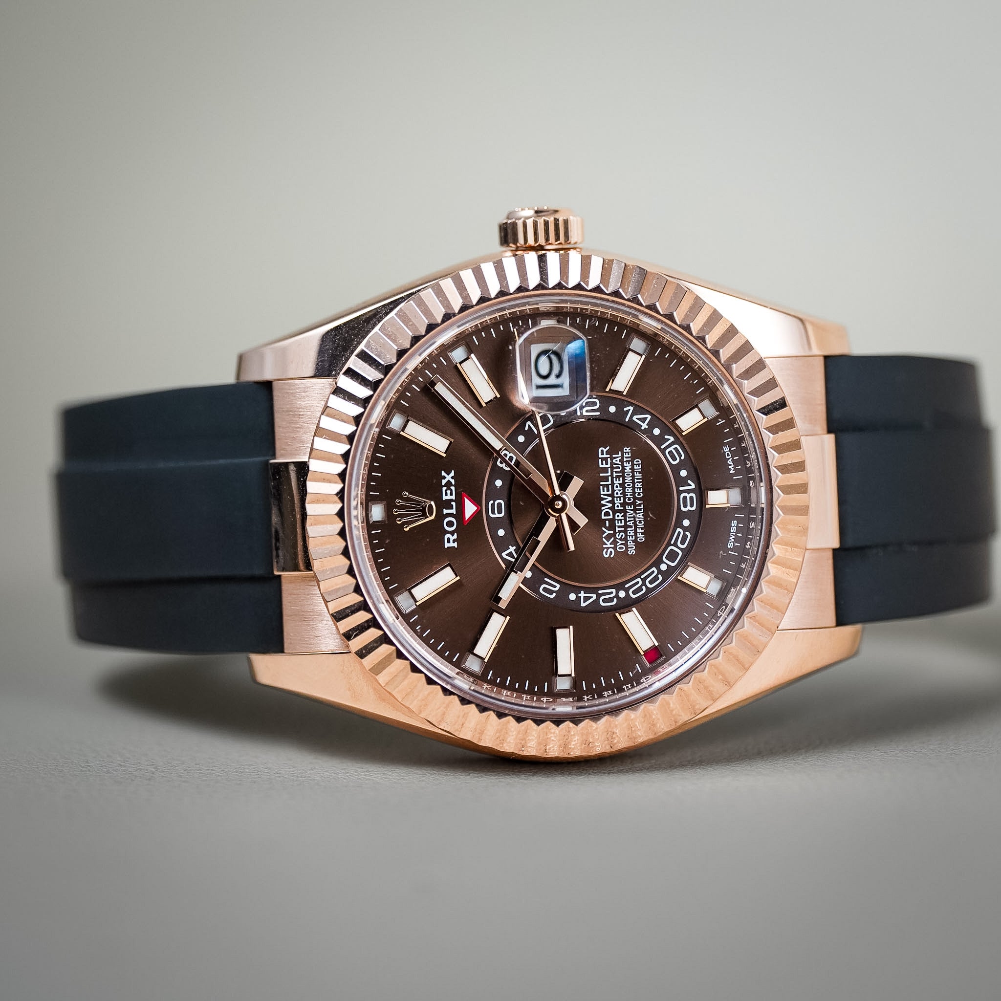 A luxury Rolex watch with a black rubber strap laying sideways on a neutral background.