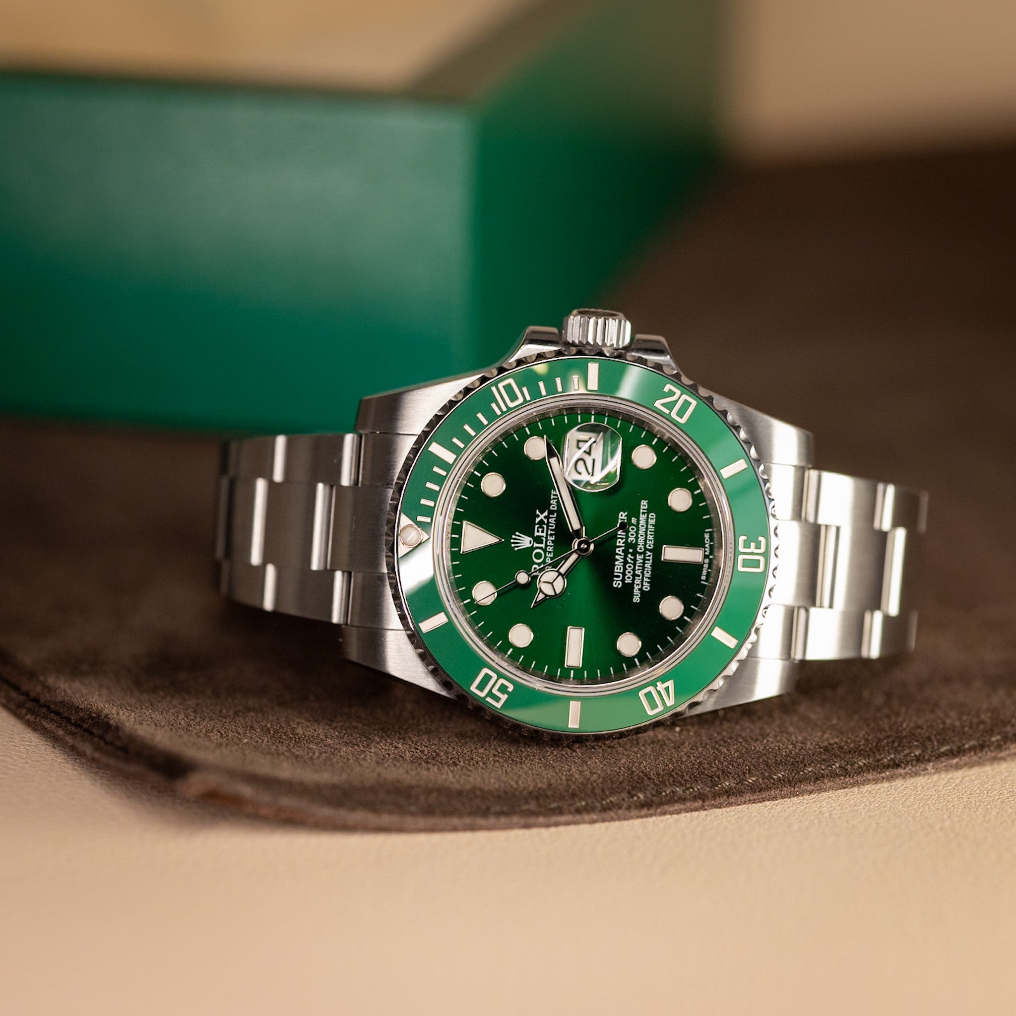 Green and silver watch on a brown surface with a blurred green background