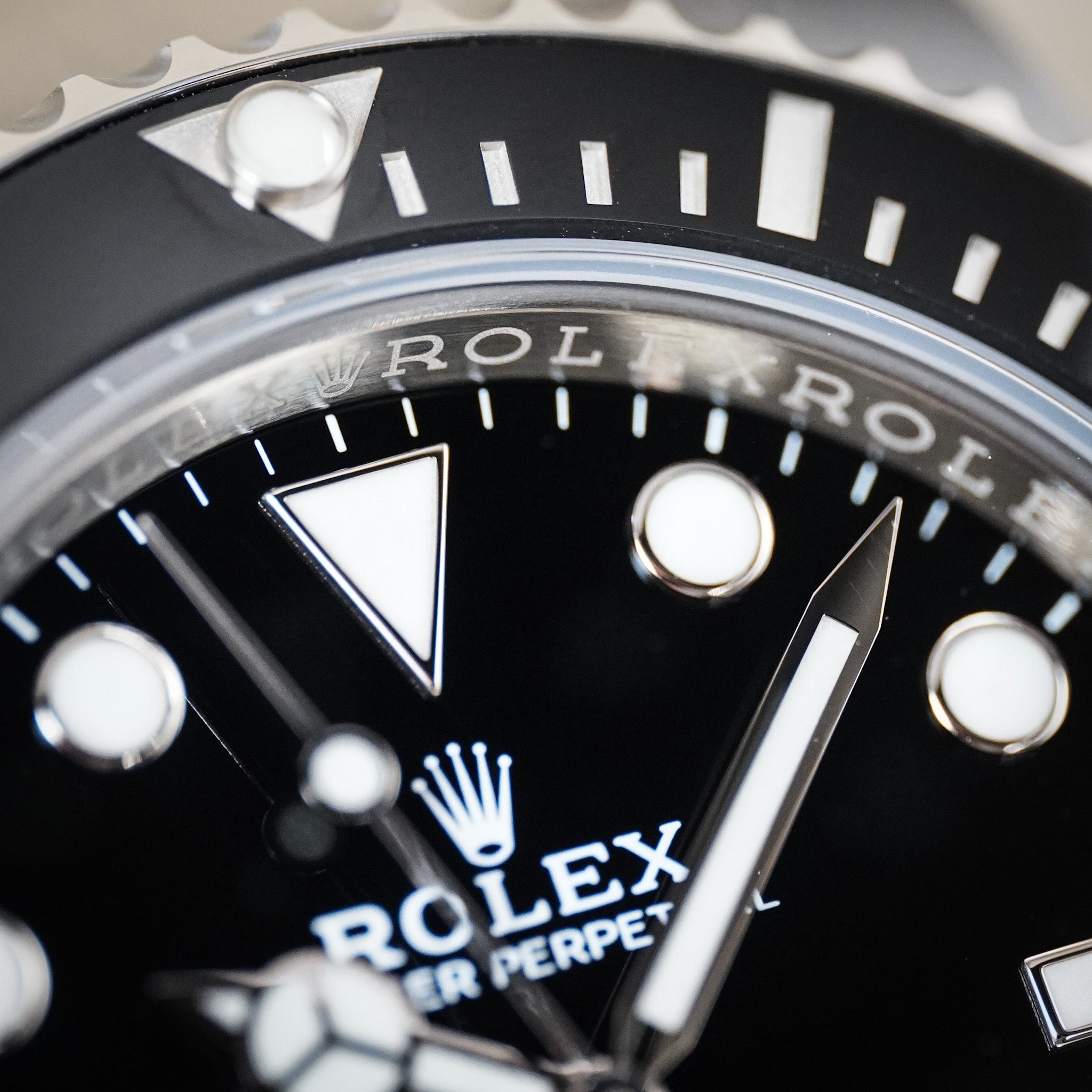 Close-up of a Rolex Submariner Perpetual watch dial with a black face, white hour markers, silver hands, and the Rolex crown logo.