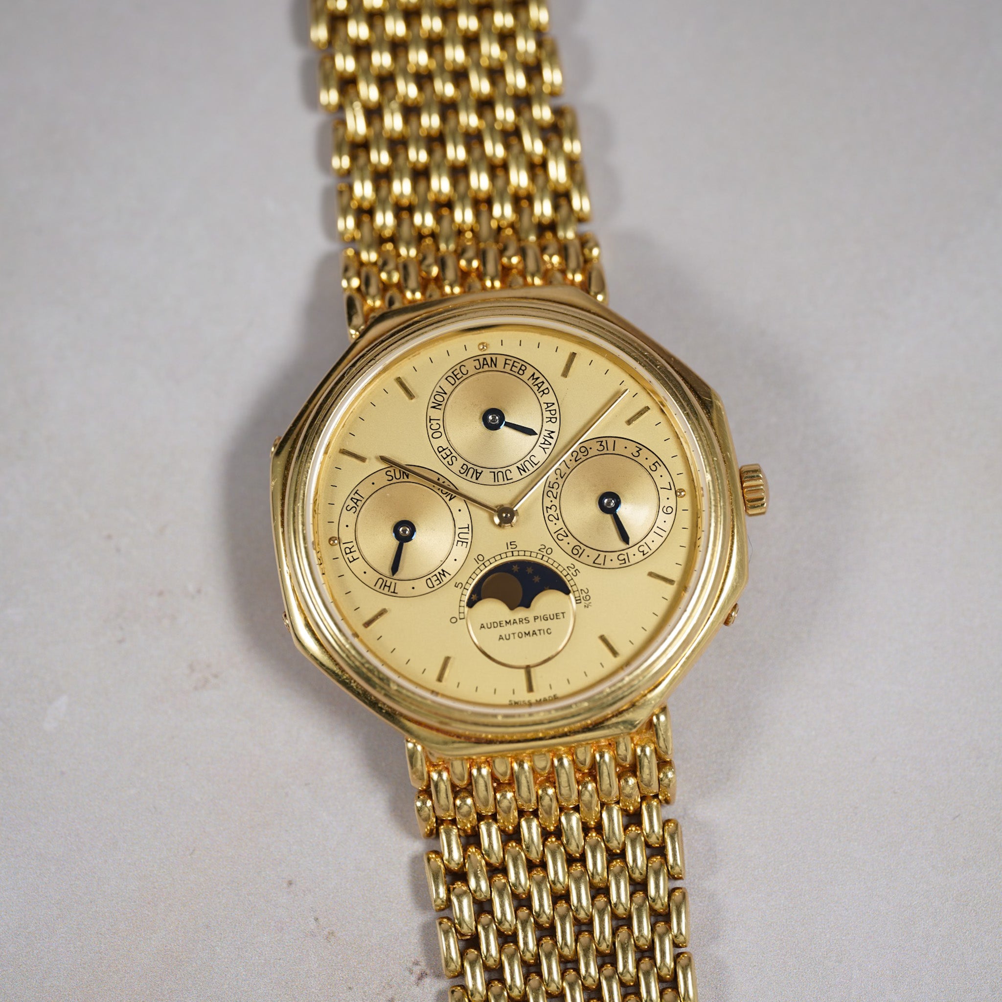 A vintage gold-tone wristwatch with a matching mesh metal bracelet, featuring a cream-colored dial with multiple subdials and a moonphase indicator.