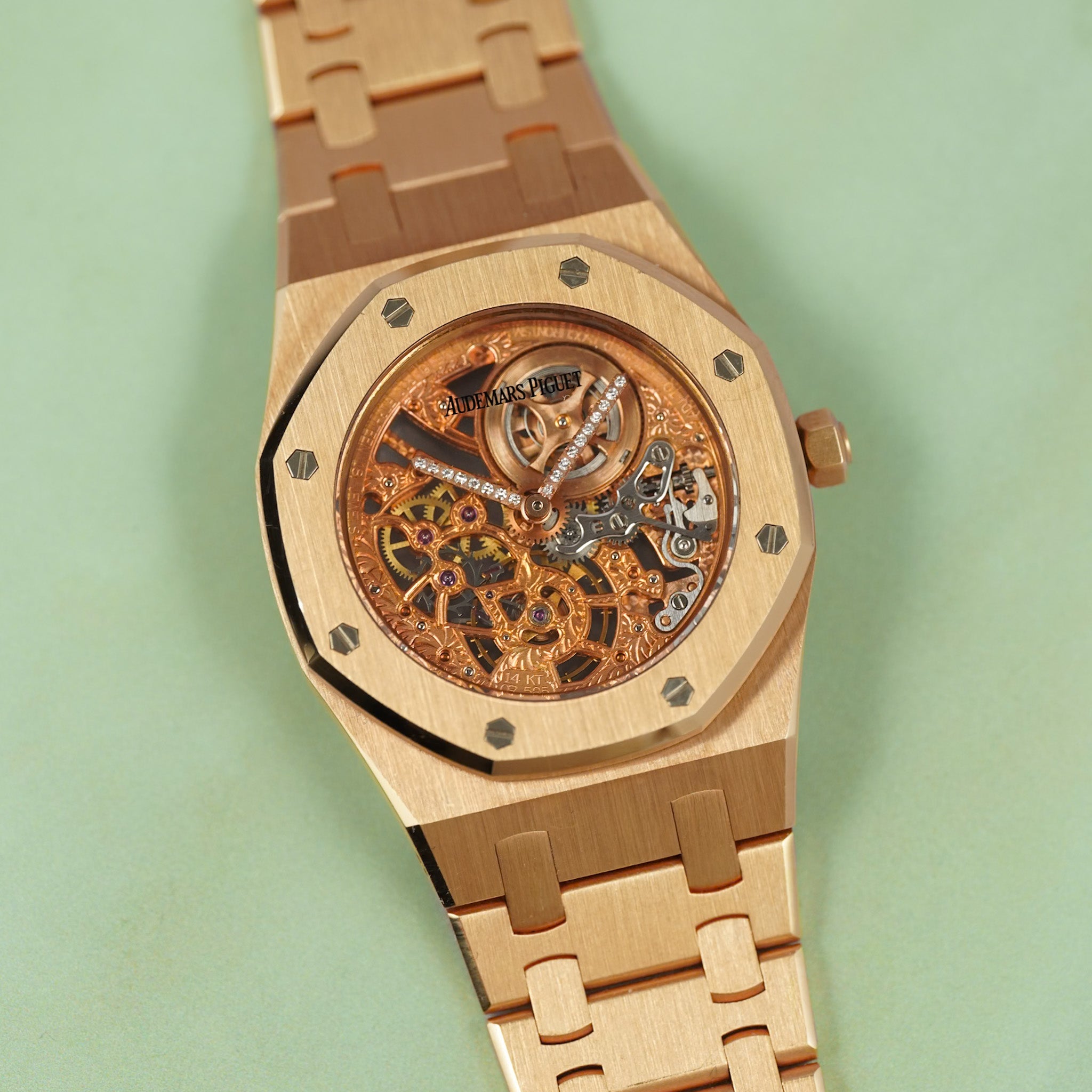 A close-up of a luxury watch with a brushed rose gold metal case and integrated bracelet, featuring a skeleton dial that reveals an intricate gold and rose gold mechanical movement. The brand name 'Audemars' is visible on the dial.