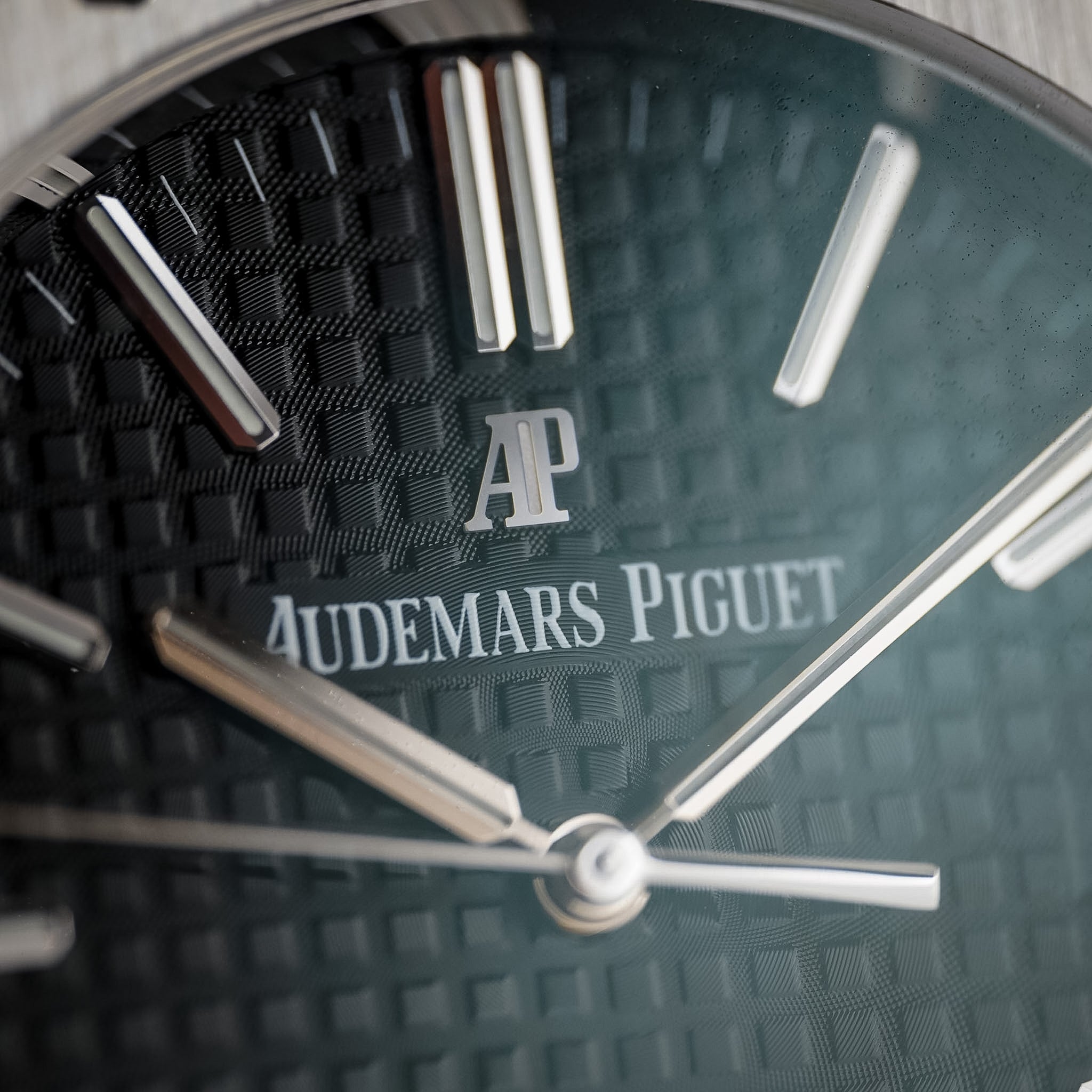 Close-up of an Audemars Piguet watch dial with a textured dark green-black face, silver baton indices, and the brand's AP logo and text.