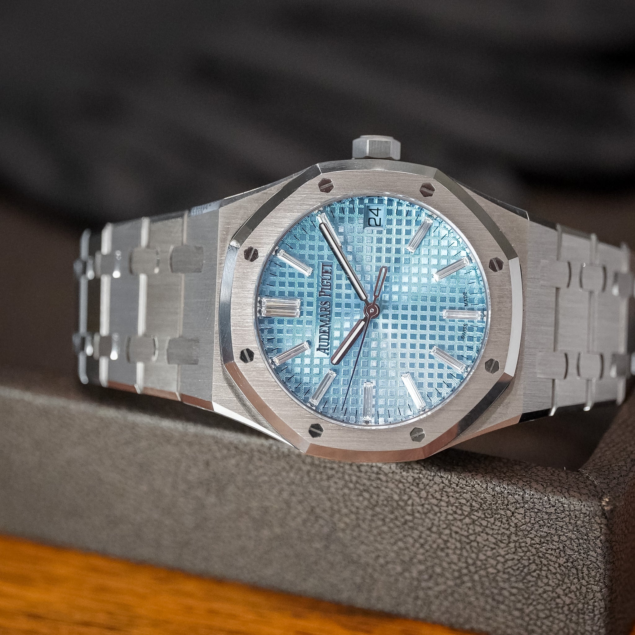 A white gold luxury watch with an ice blue dial laying sideways on a dark brown tray