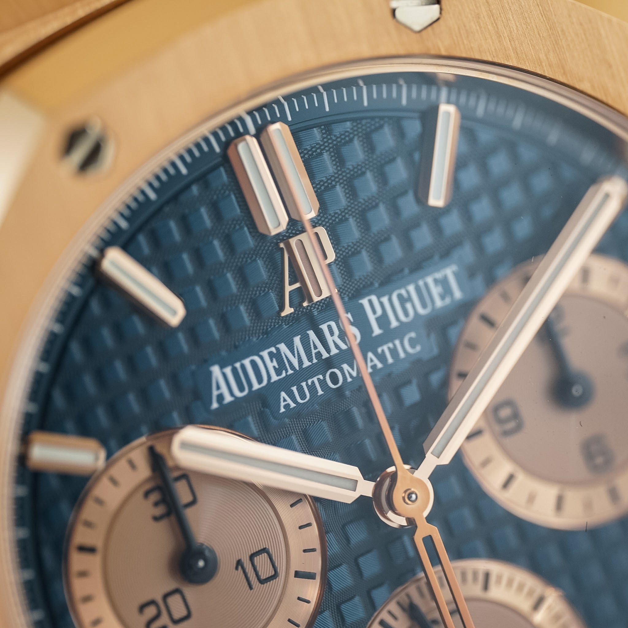 Close-up of an Audemars Piguet Automatic watch featuring a textured blue dial, rose gold-toned markers and hands, and a gold-toned bezel.