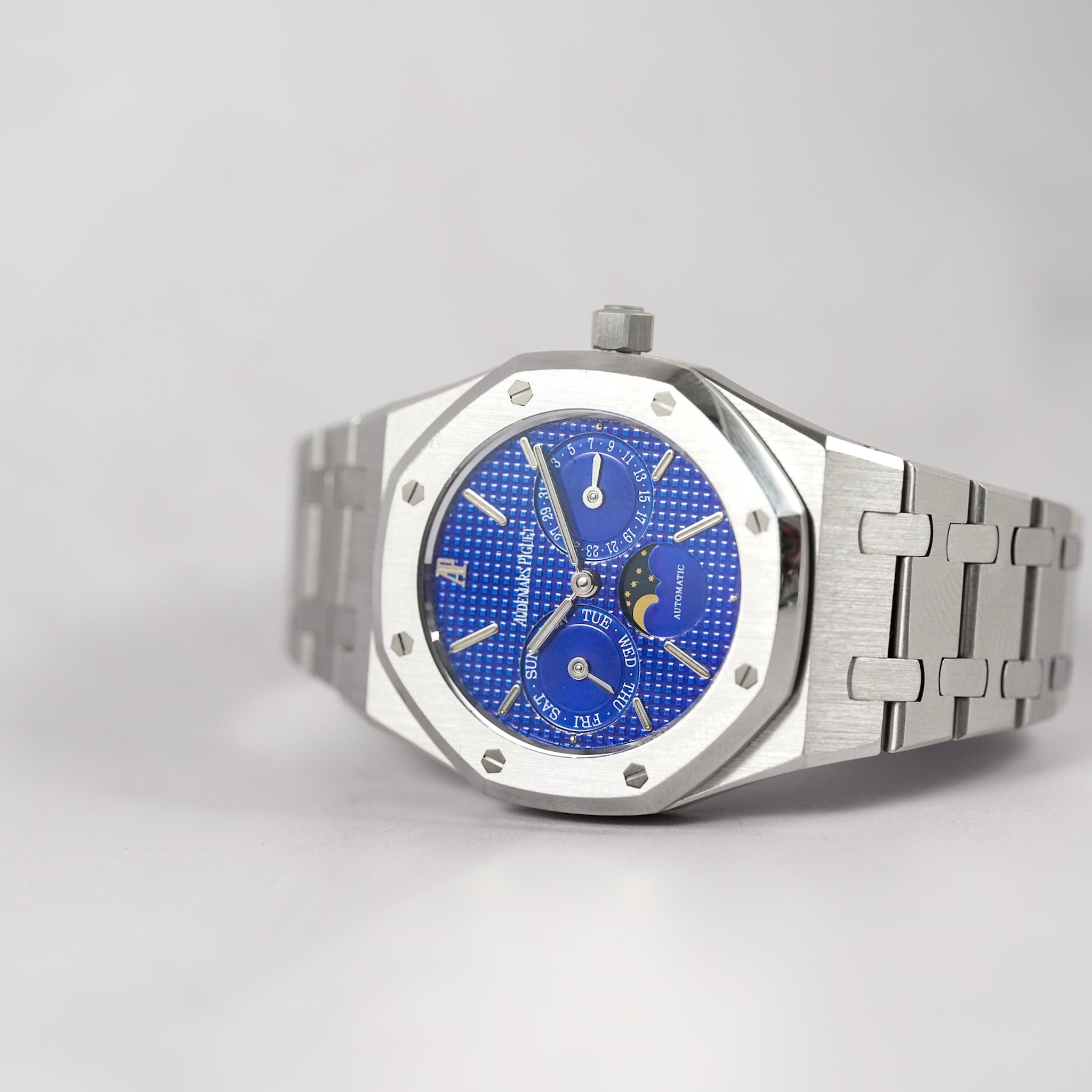 A luxury stainless steel wristwatch with an octagonal bezel and a vibrant blue textured dial featuring moonphase indicators, shown on a light gray background.