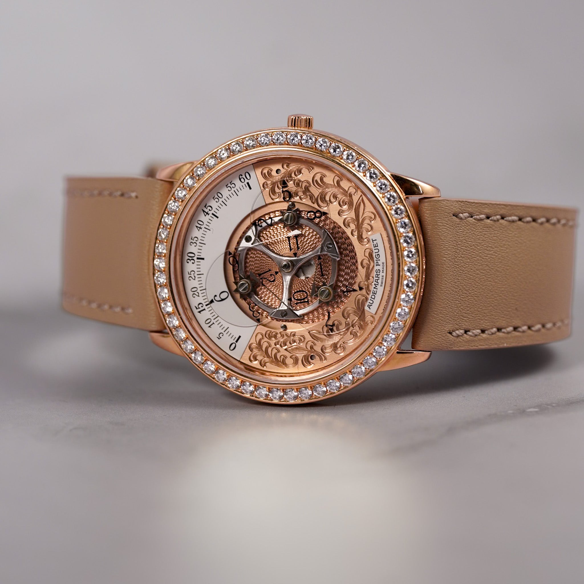 A luxury skeleton watch with a rose gold case, crystal-studded bezel, and tan leather strap, displayed on a neutral gray background.
