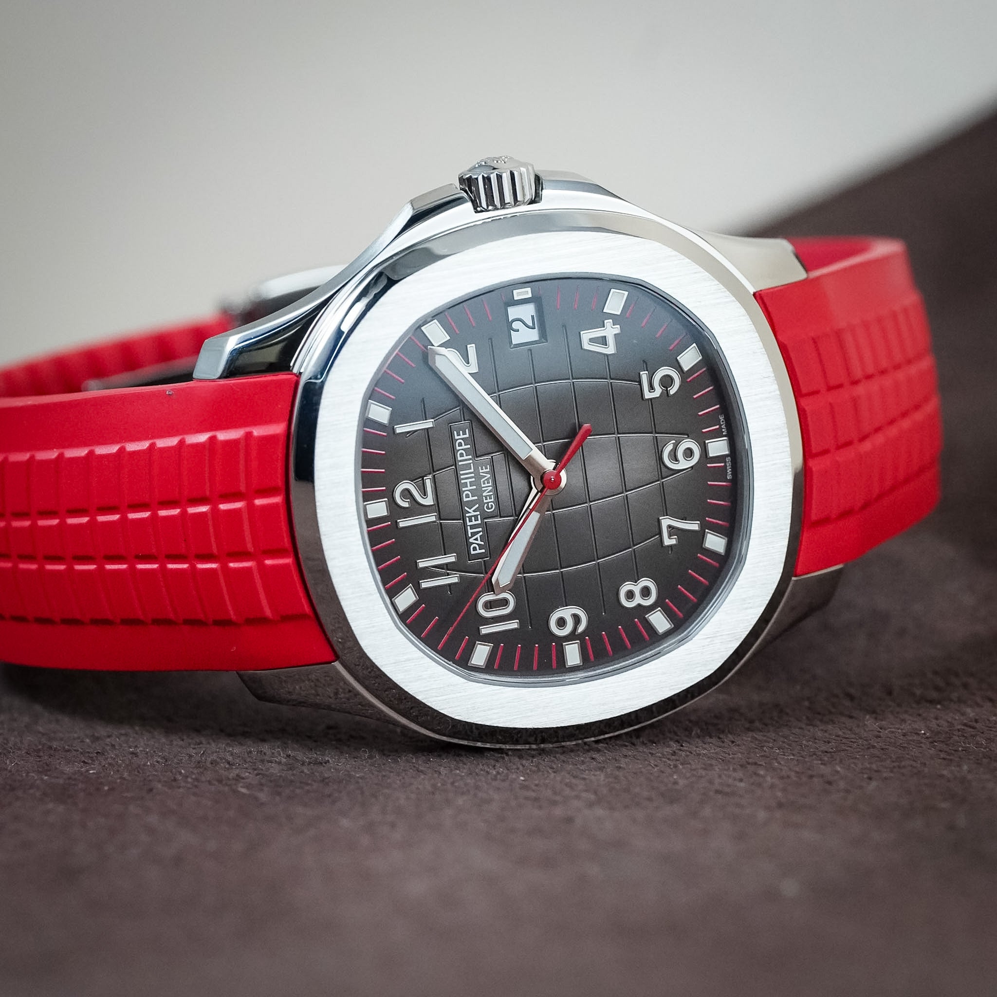 A close-up shot of a Patek Philippe Nautilus watch featuring a bold red rubber strap, a silver-toned stainless steel case, and a dark gray grid-patterned dial with white Arabic numerals.