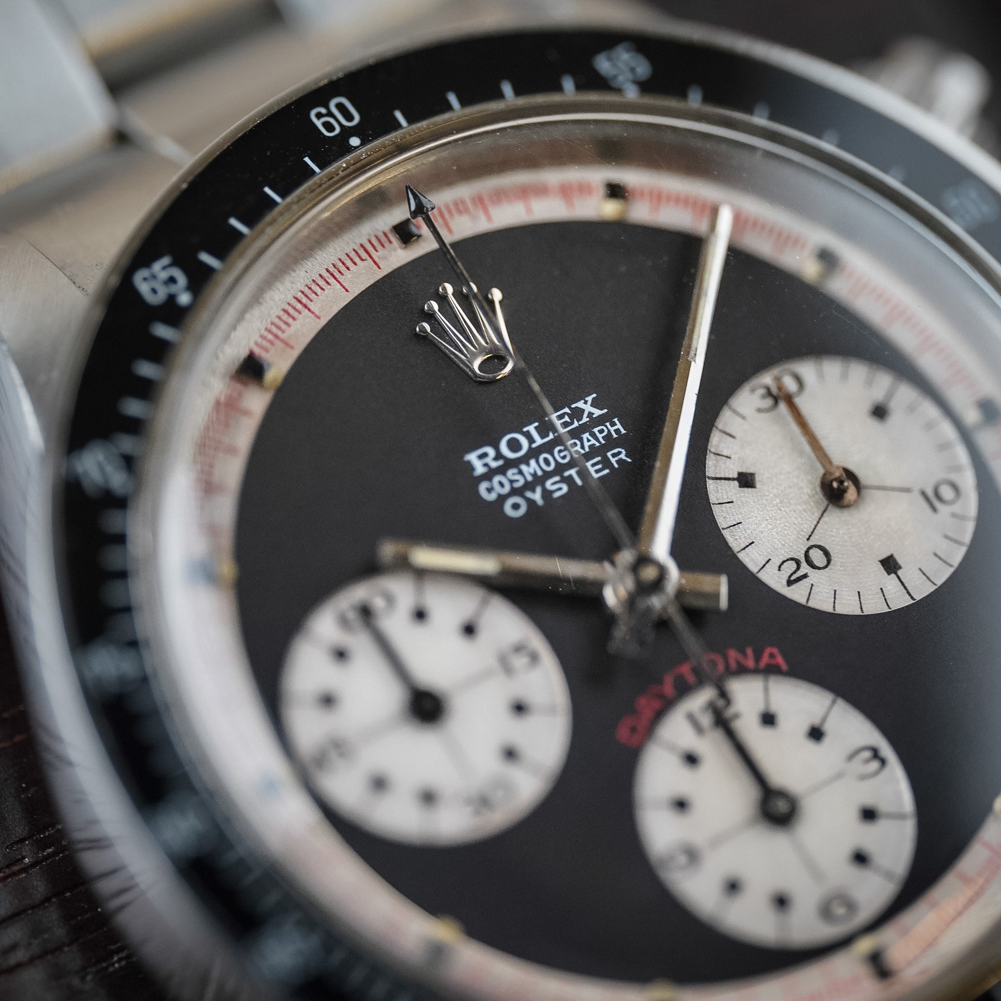 Closeup of a  black dial vintage Rolex Daytona in steel with a black bezel, white subdials, and red accents. The words Rolex Cosmograph Oyster and Daytona are visible.