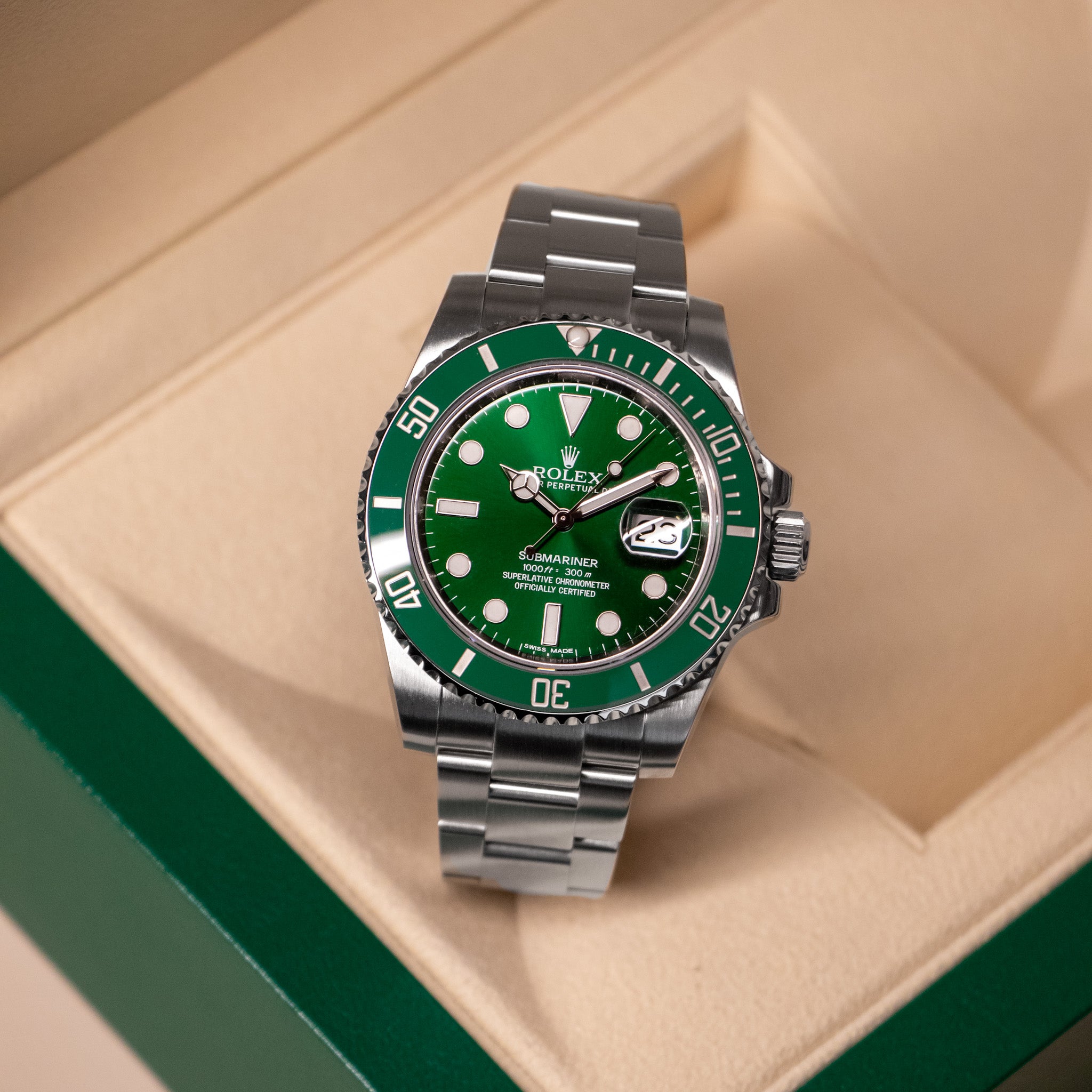 Green and silver watch on a beige cushion