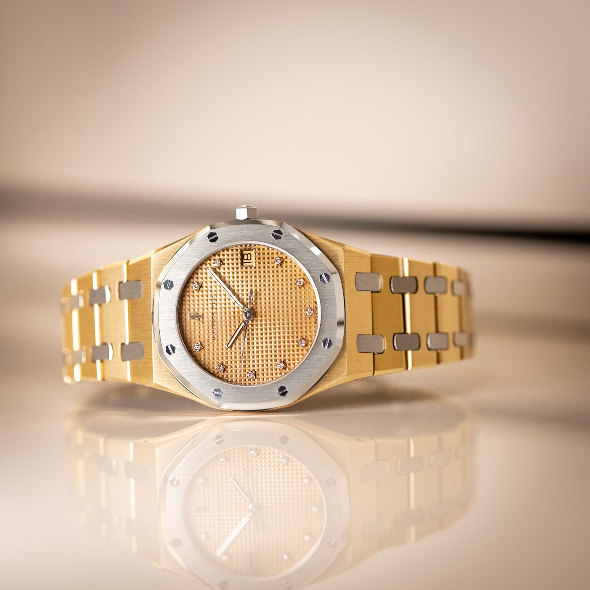 Gold and silver watch on a reflective surface with a beige background