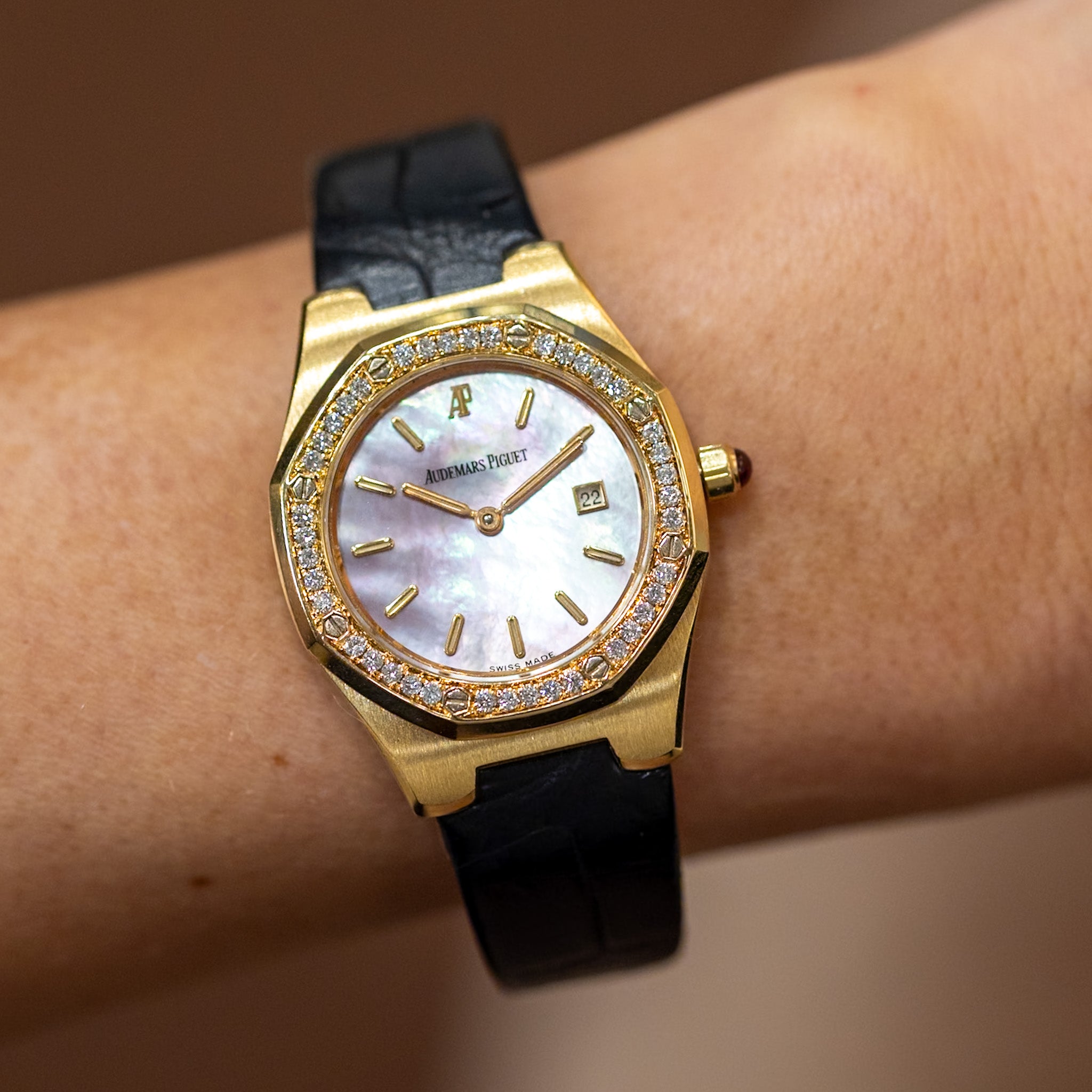 Gold watch with black strap on a wrist against a blurred background