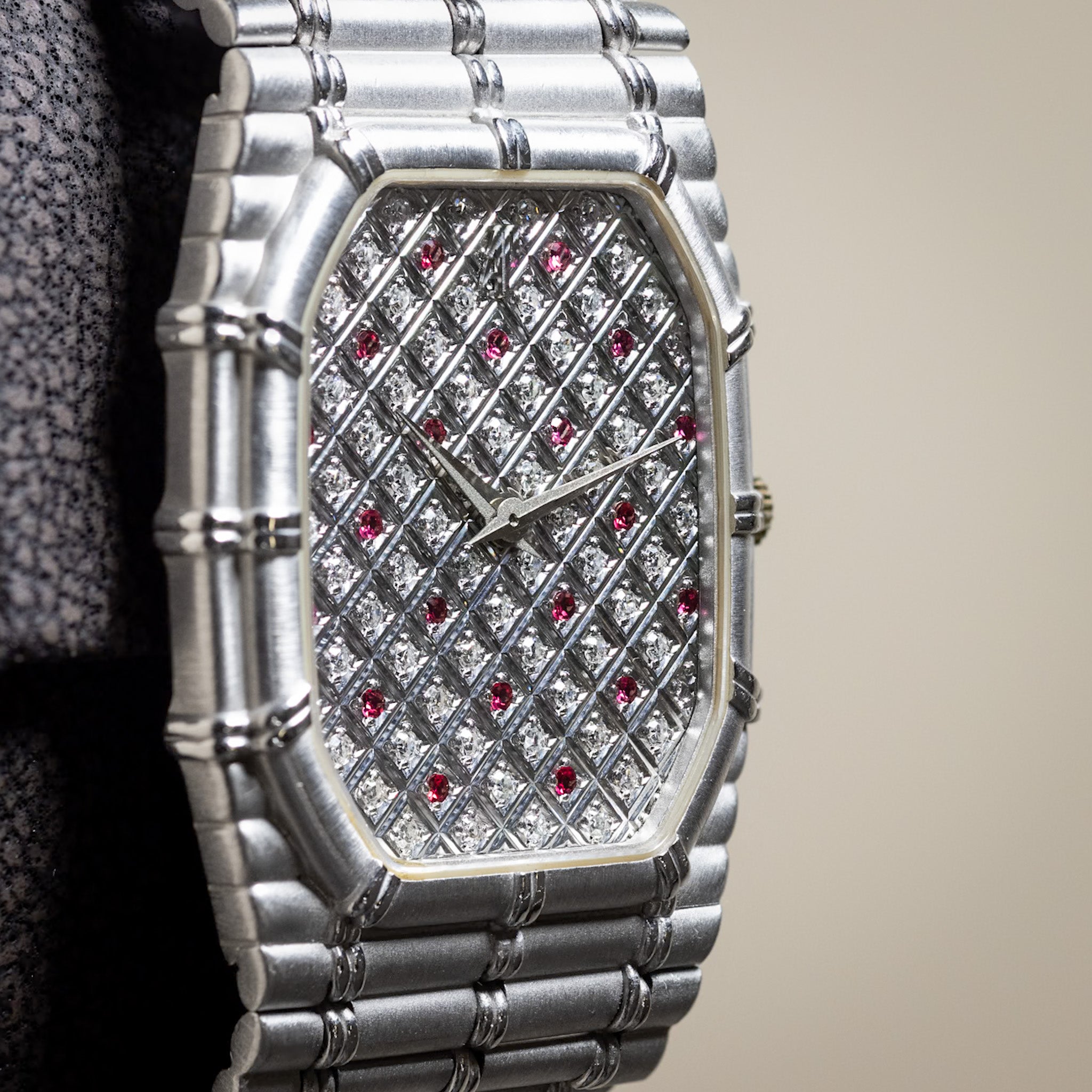 Luxury silver watch with diamond and ruby accents on a blurred background