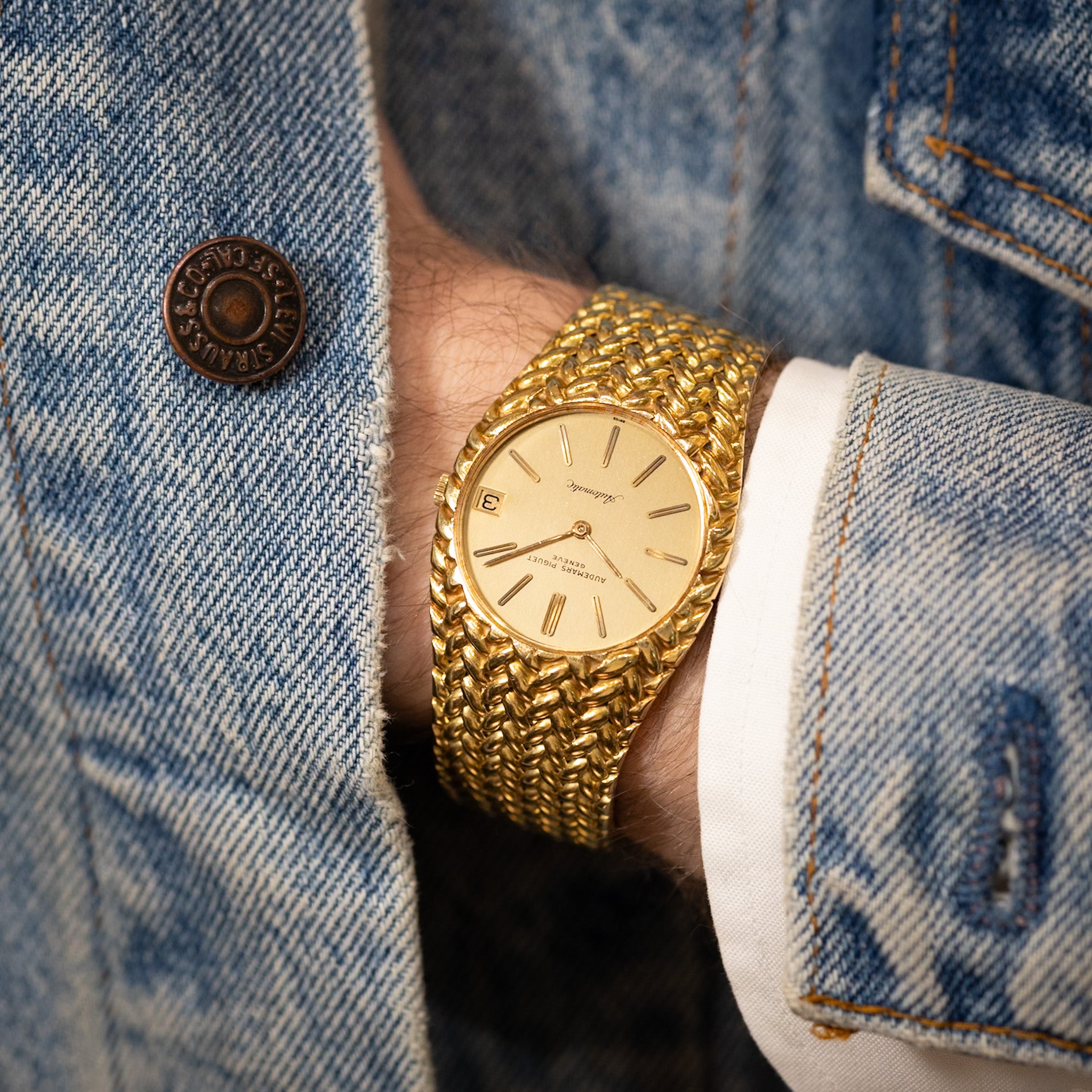 Gold wristwatch on a person wearing a denim jacket.