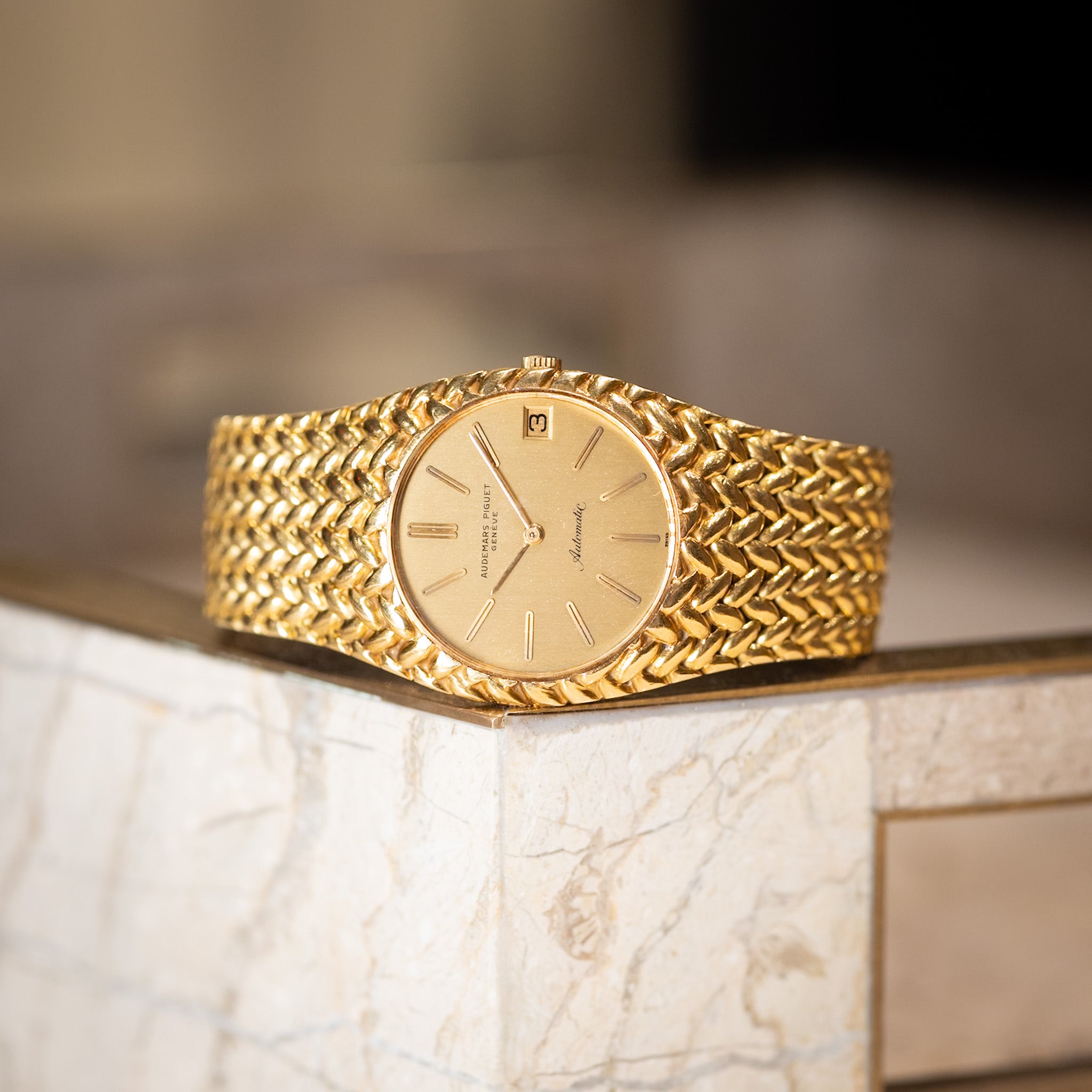 Gold wristwatch with braided design on a marble surface