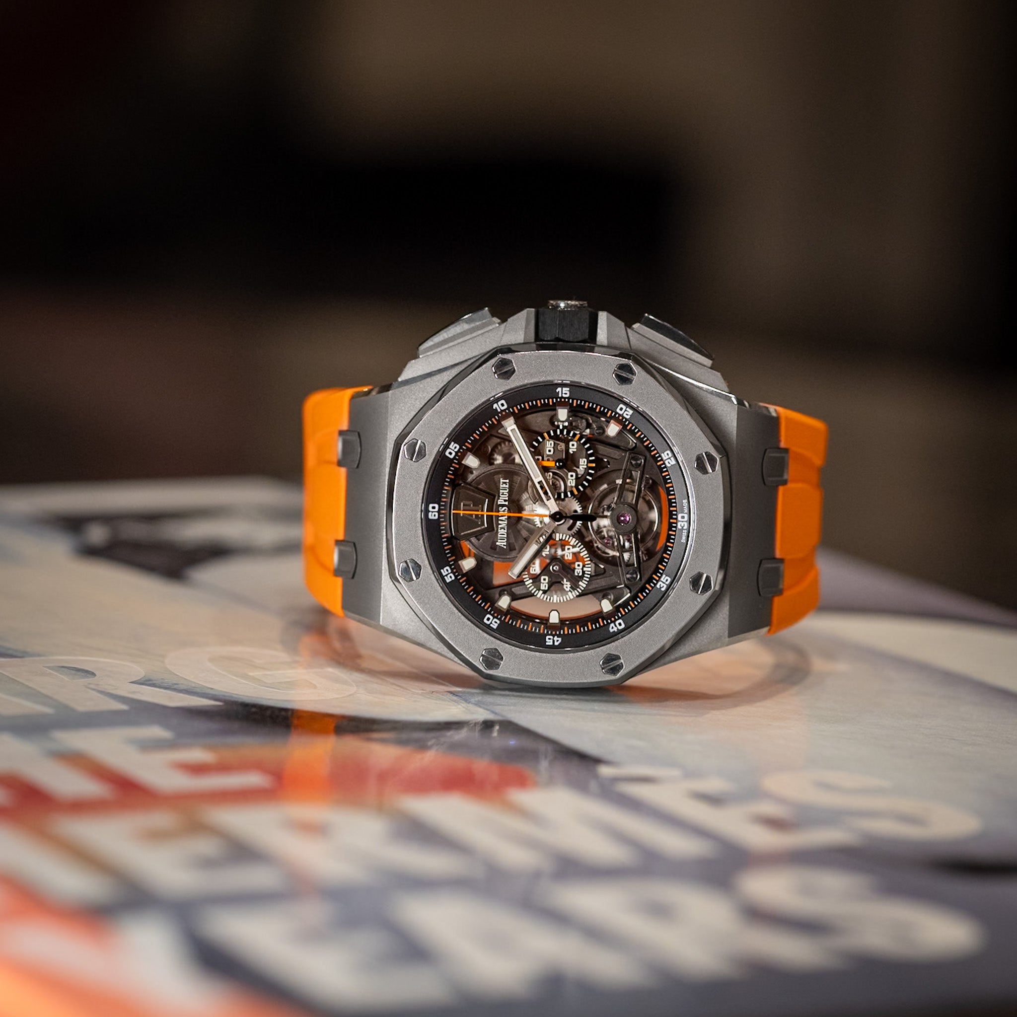 Luxury watch with orange and silver design on a blurred newspaper background