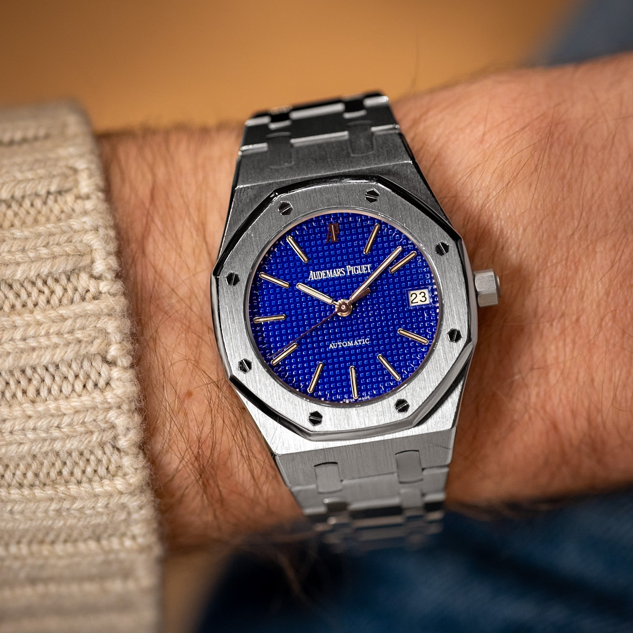 Luxury watch with blue dial and silver metal strap on a wrist.