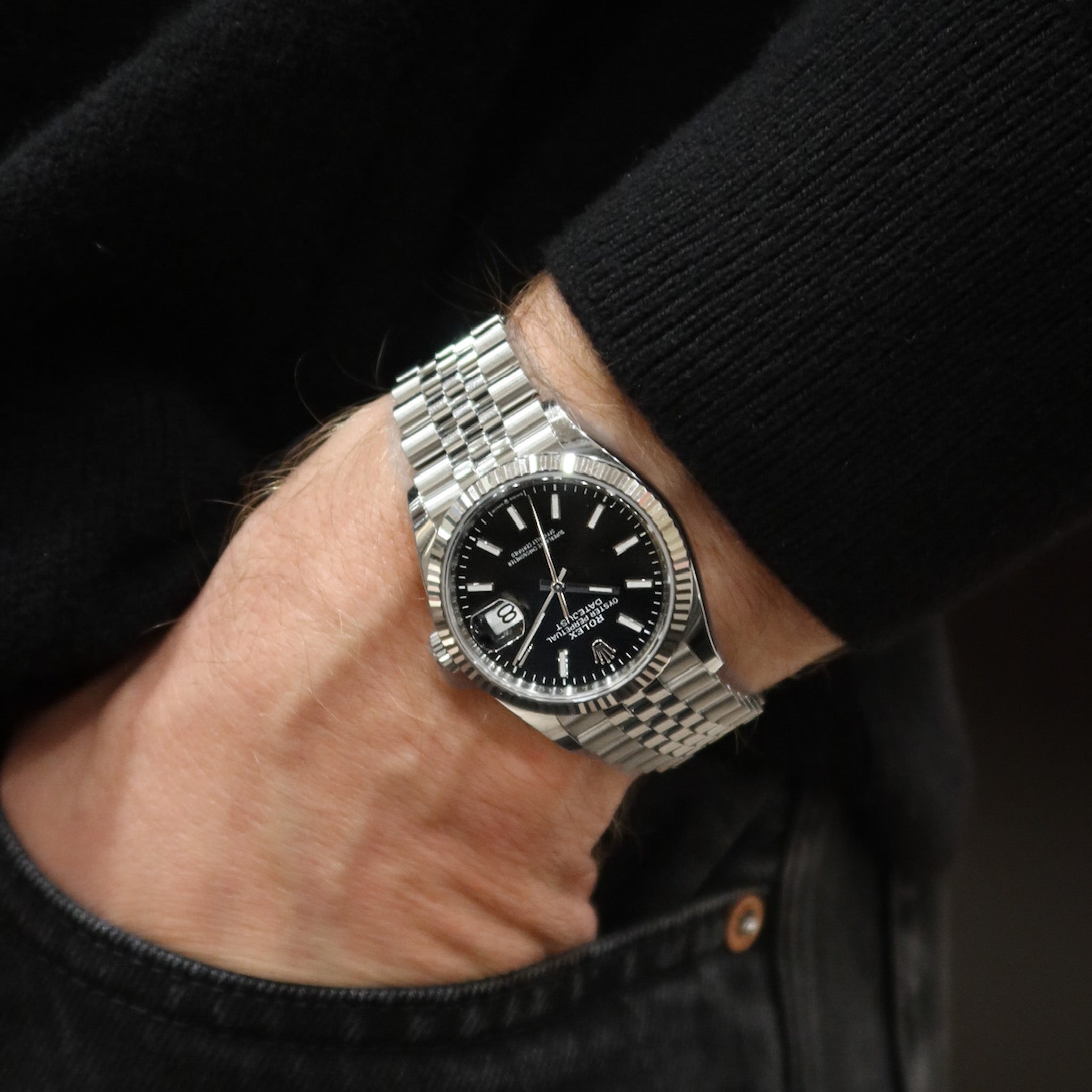 Silver watch with a black face on a person's wrist against a dark background