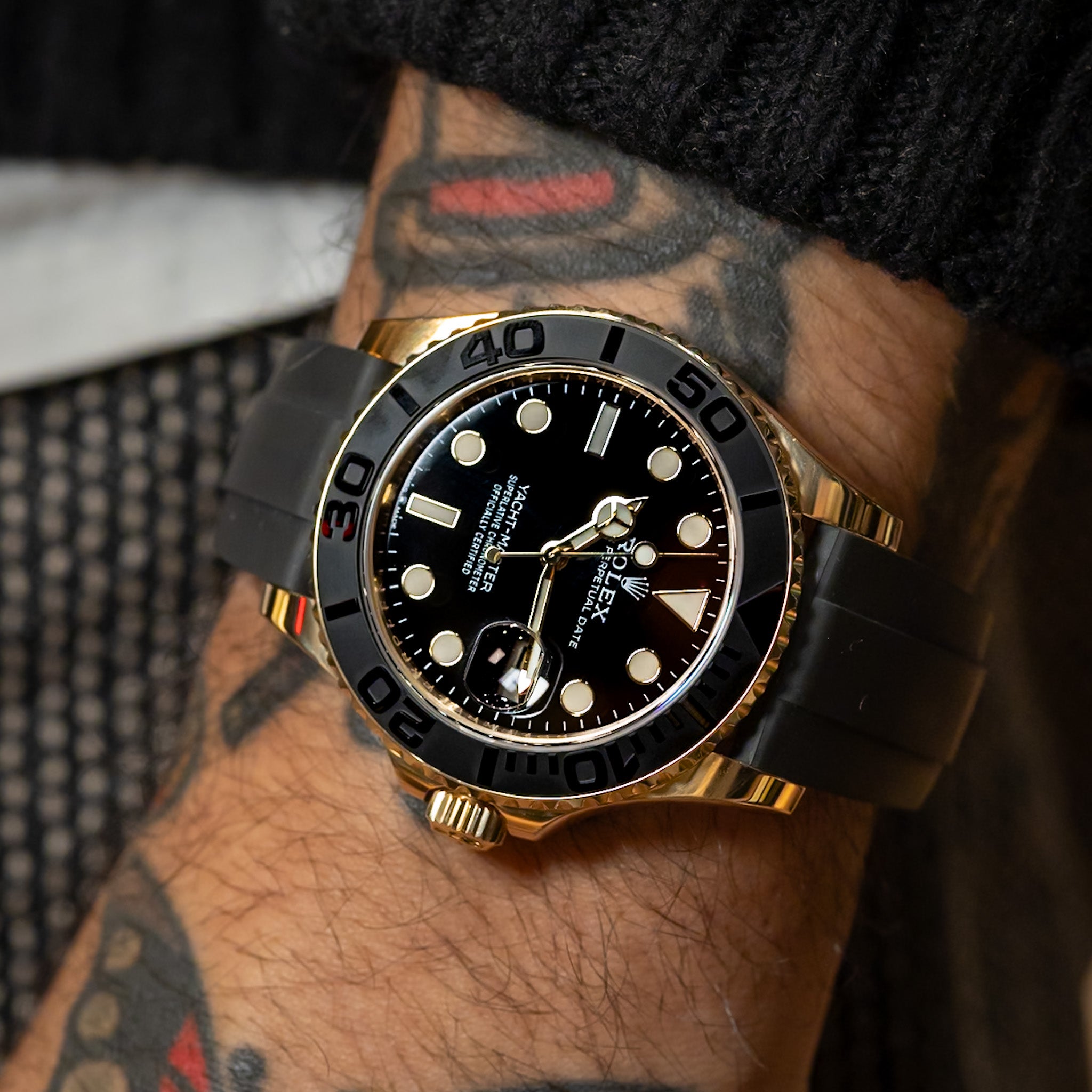 Luxury watch with black dial and gold accents on a wrist with tattoos. 