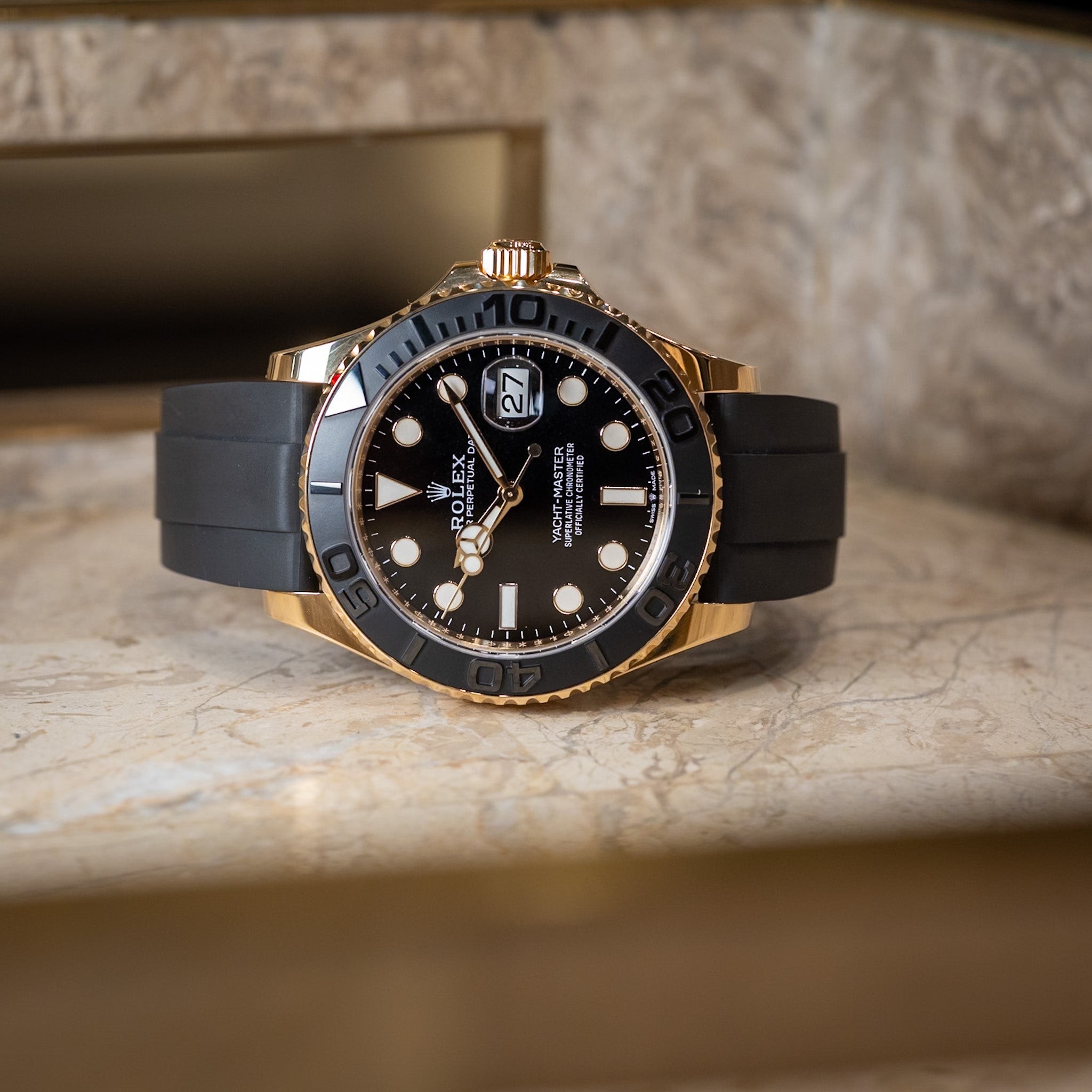 Luxury watch with black rubber strap and gold casing on a marble surface